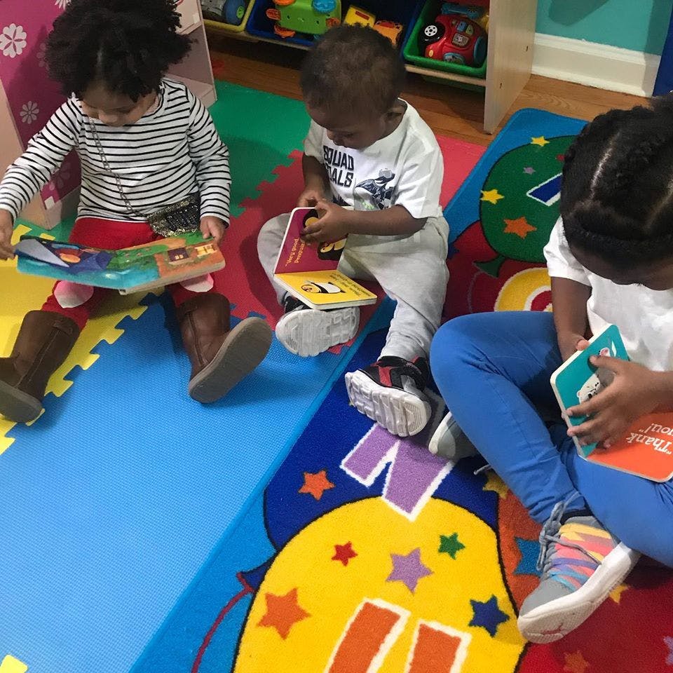 Three children sitting on a colorful mat, each holding and looking at a book