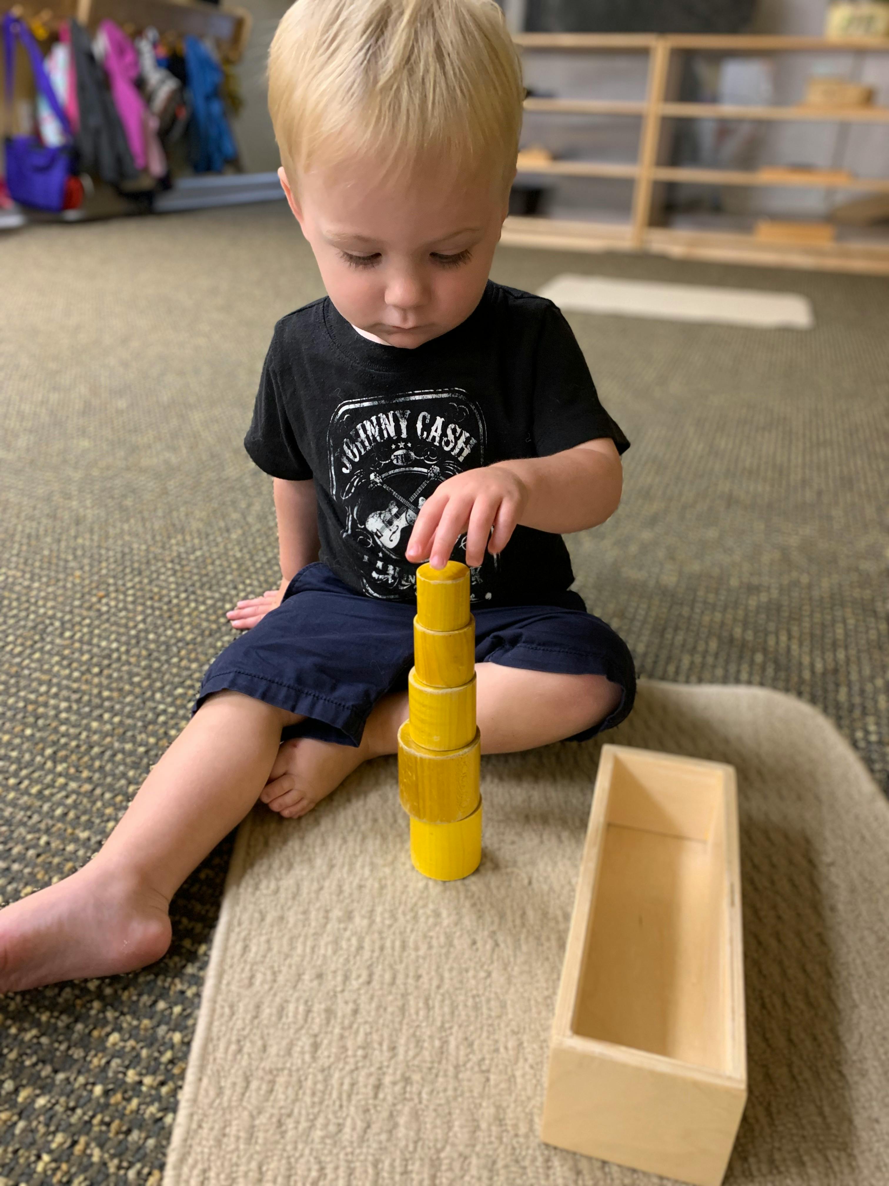 Child sitting on floor playing with yellow stacking toy