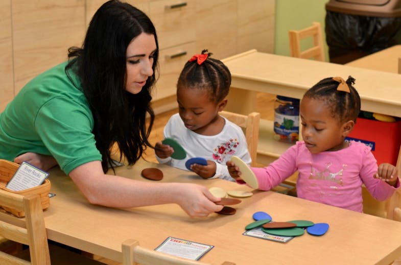 Person and two children playing with colorful shapes at a table