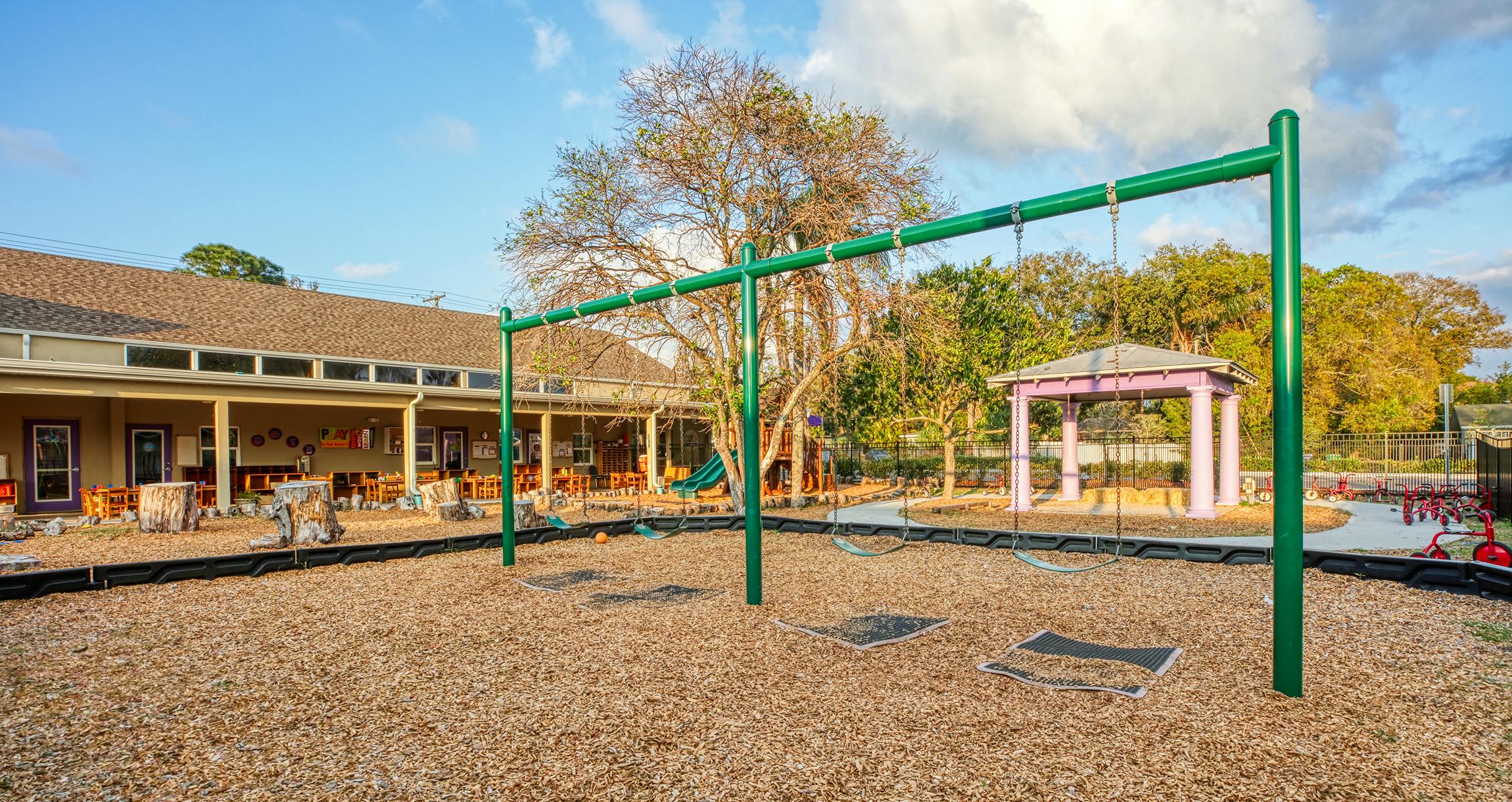 Empty outdoor playground with a green swing set and wooden chips on a sunny day