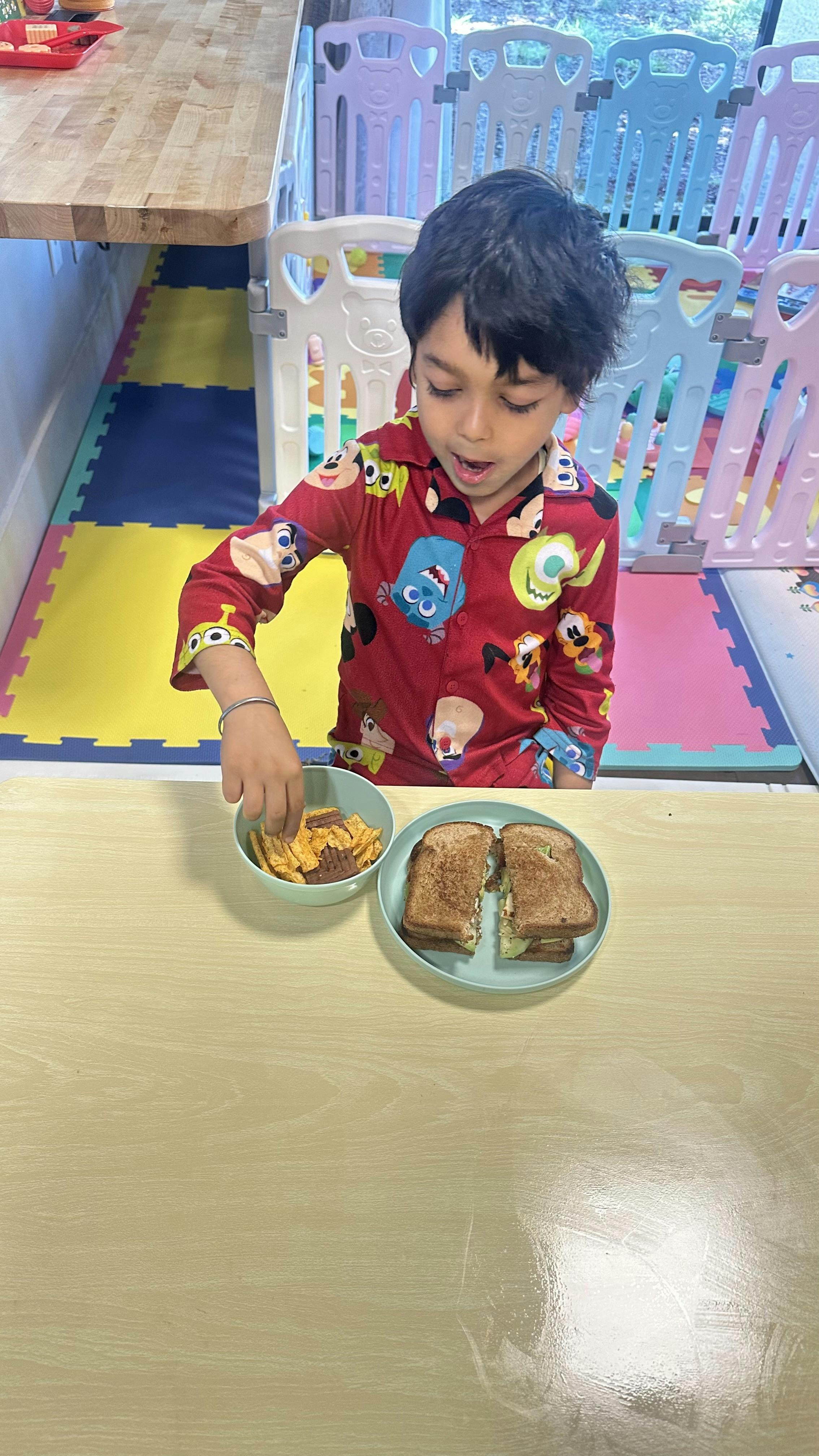 Child reaching for food in a bowl next to a plate of sandwiches