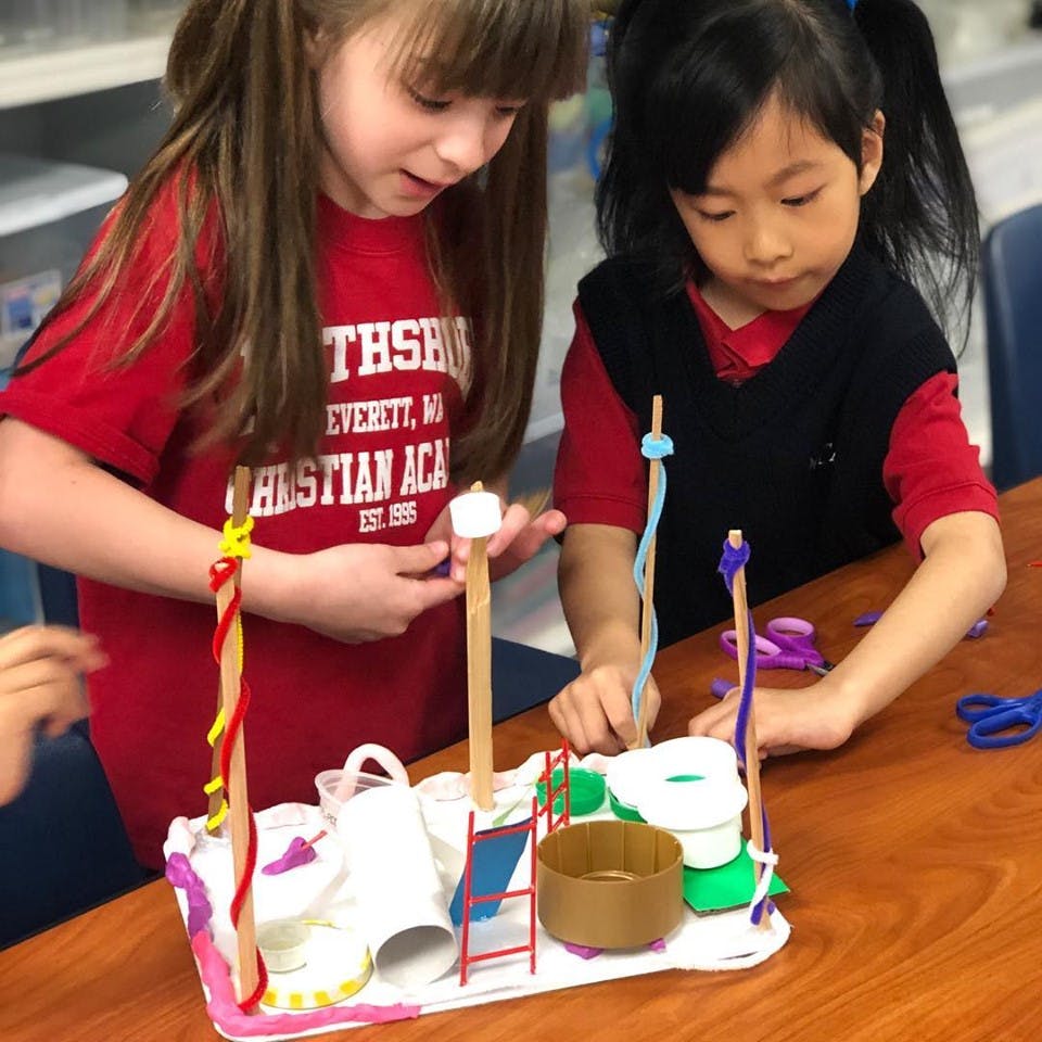 Two children working on a craft project with sticks and paper