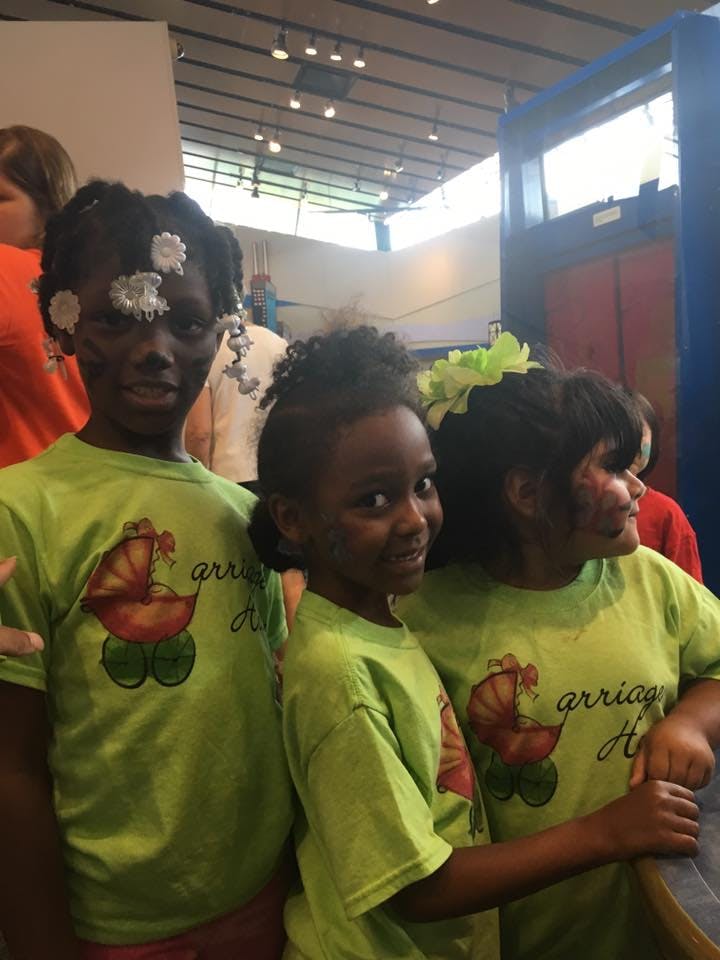 Three children in green shirts with face paint and hair decorations