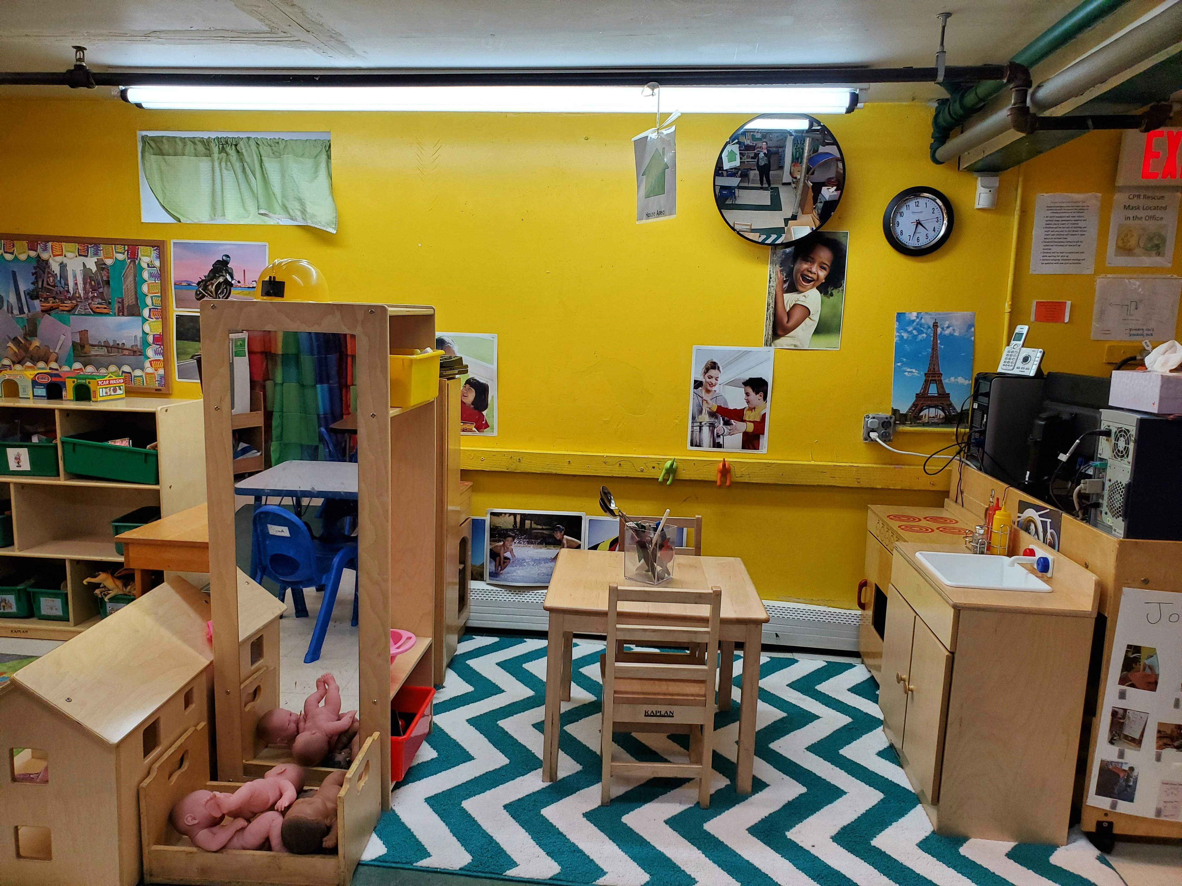 Classroom with yellow walls, small tables and chairs, and a play kitchen