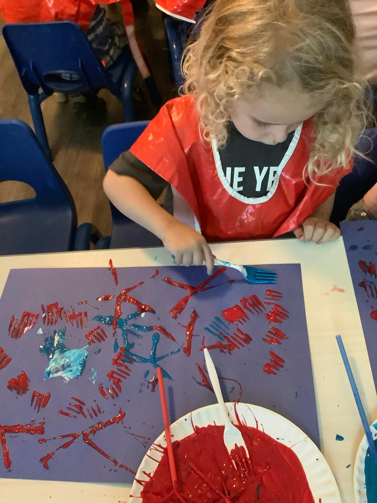 Child using a plastic fork to paint with red and blue paint on paper