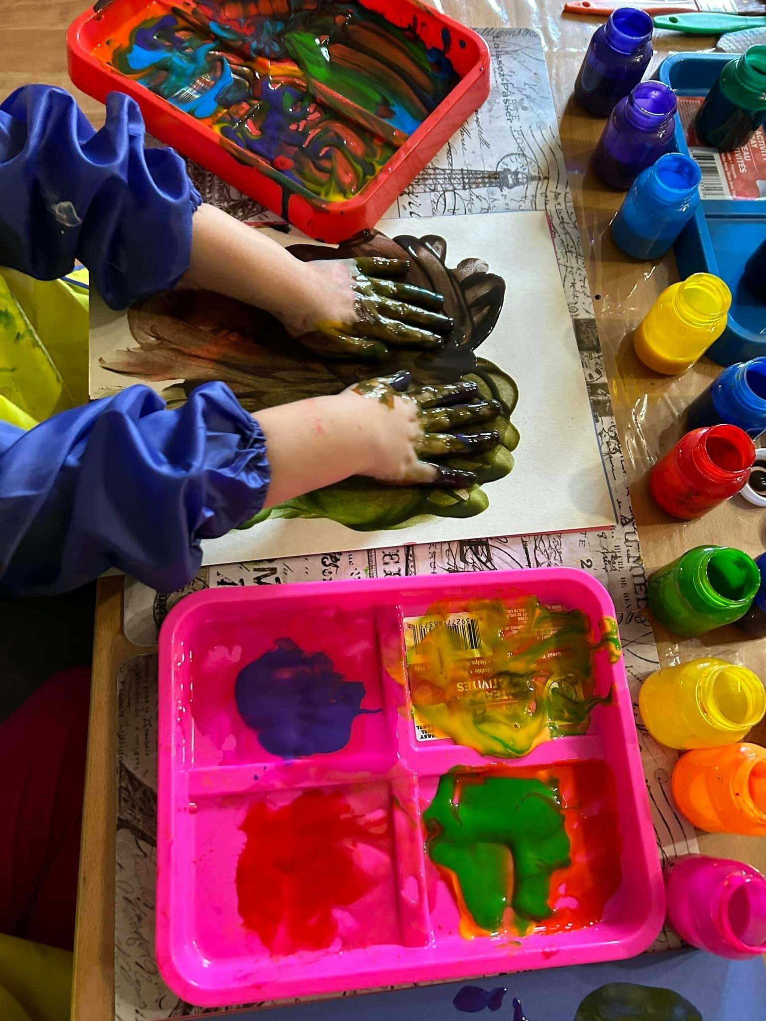 Child in blue smock finger painting with dark green and brown paint