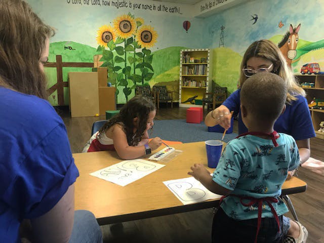 Adult and two children painting at a table in a classroom
