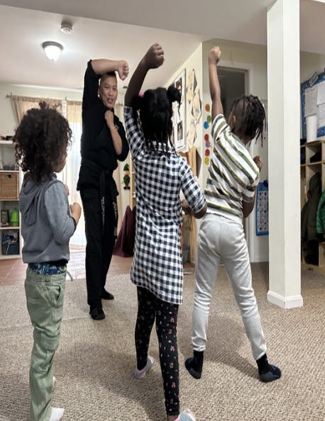 Person in black uniform teaching martial arts to three children