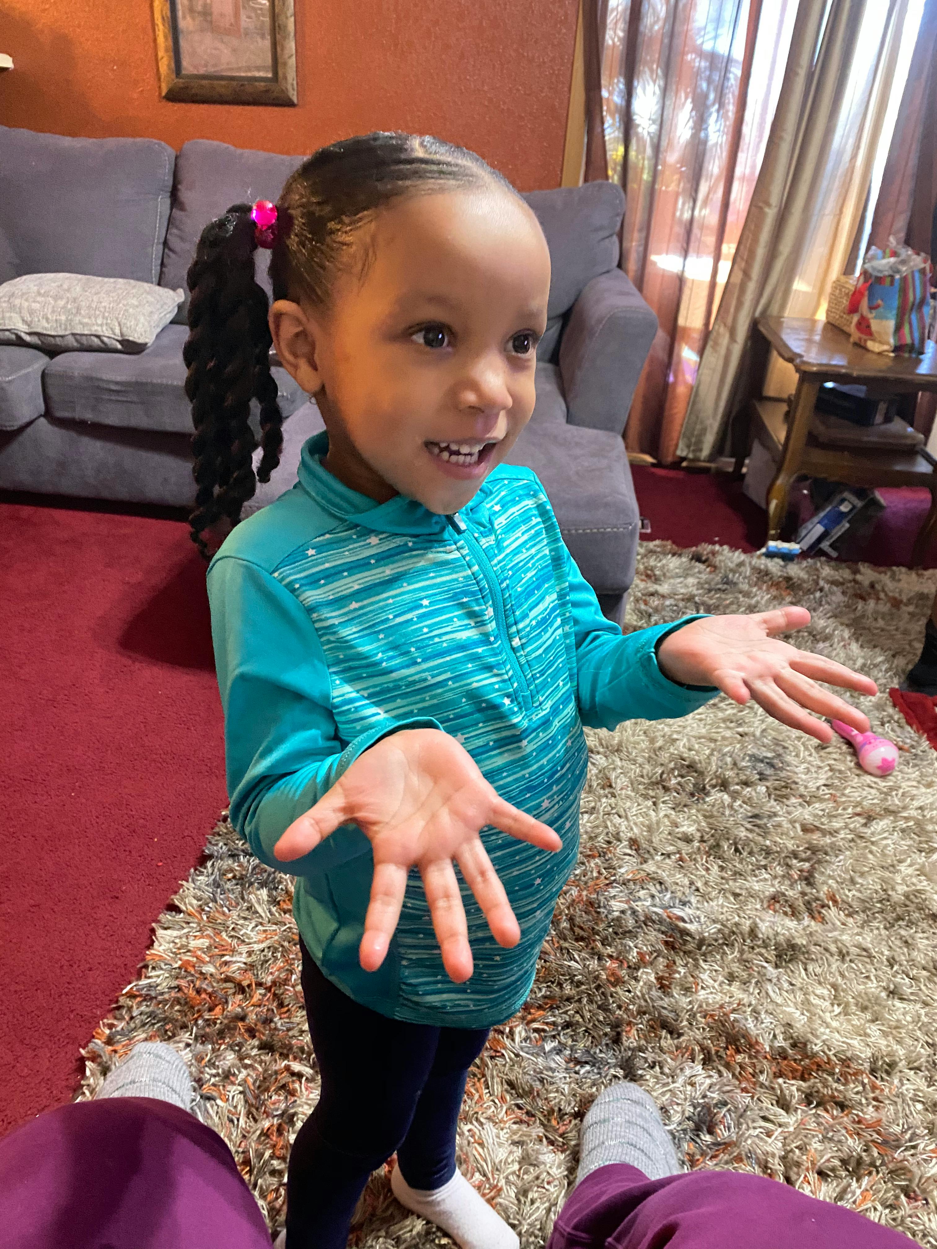 Child with braided ponytail and blue shirt holding hands out