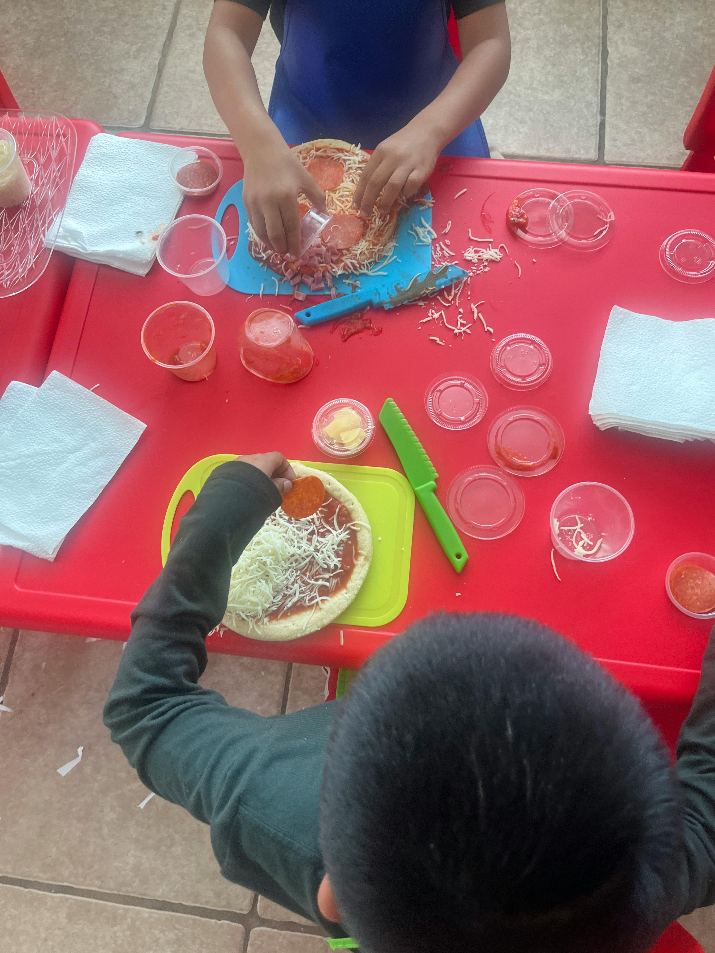 Two children making pizzas on a red table