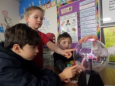 Three children interacting with a plasma ball in a classroom