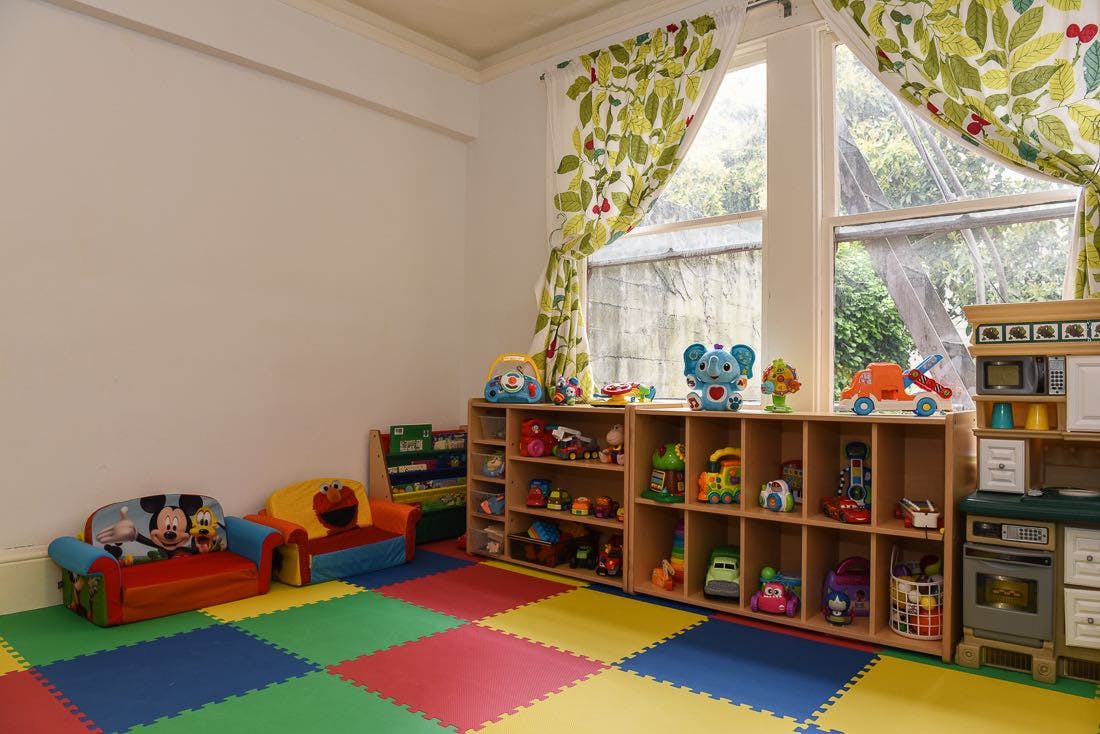 Playroom with colorful floor mats, toy shelves, and small couches