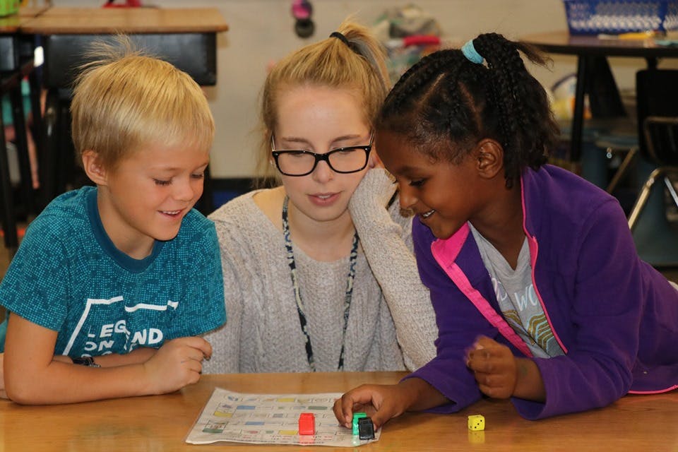 Adult and two children playing a board game in a classroom