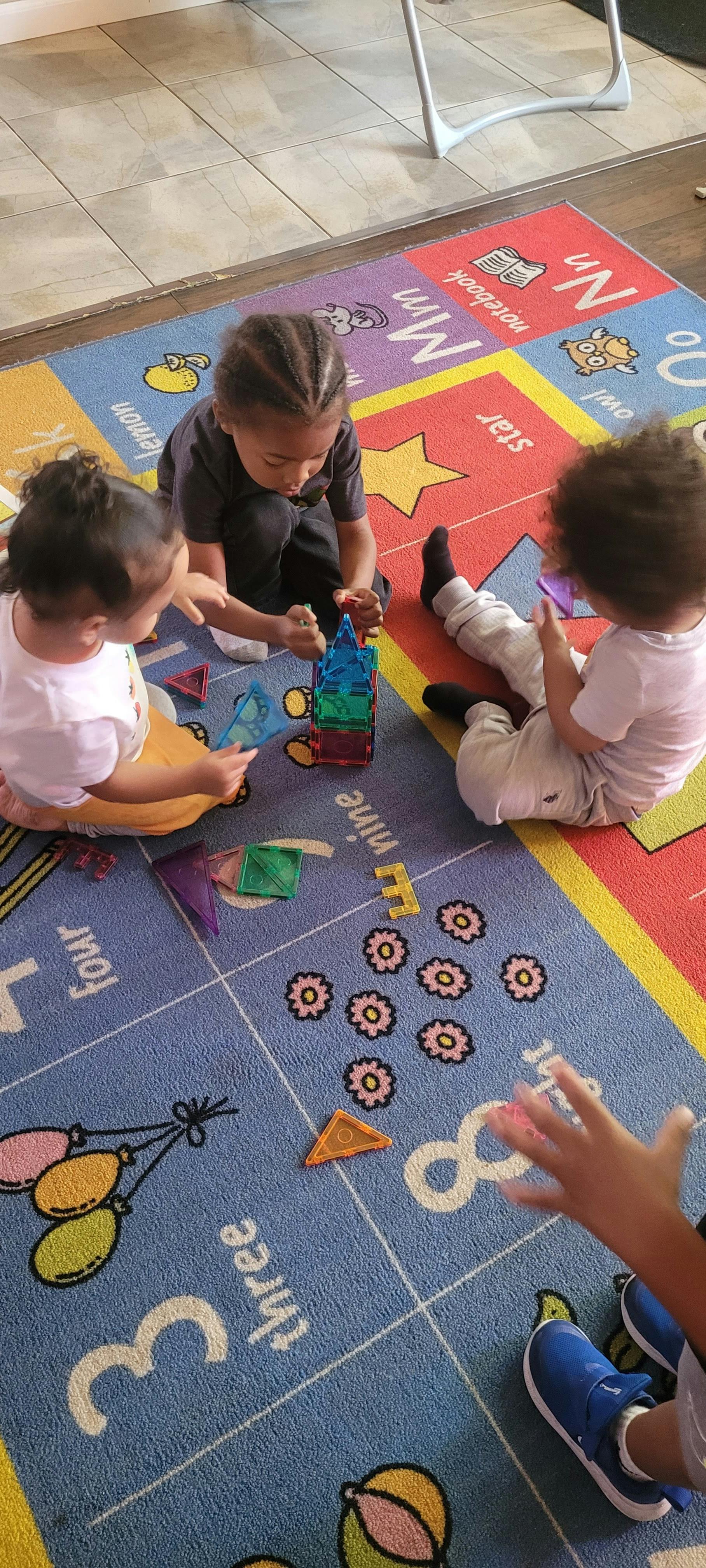 Three children playing with magnetic tiles on a colorful rug