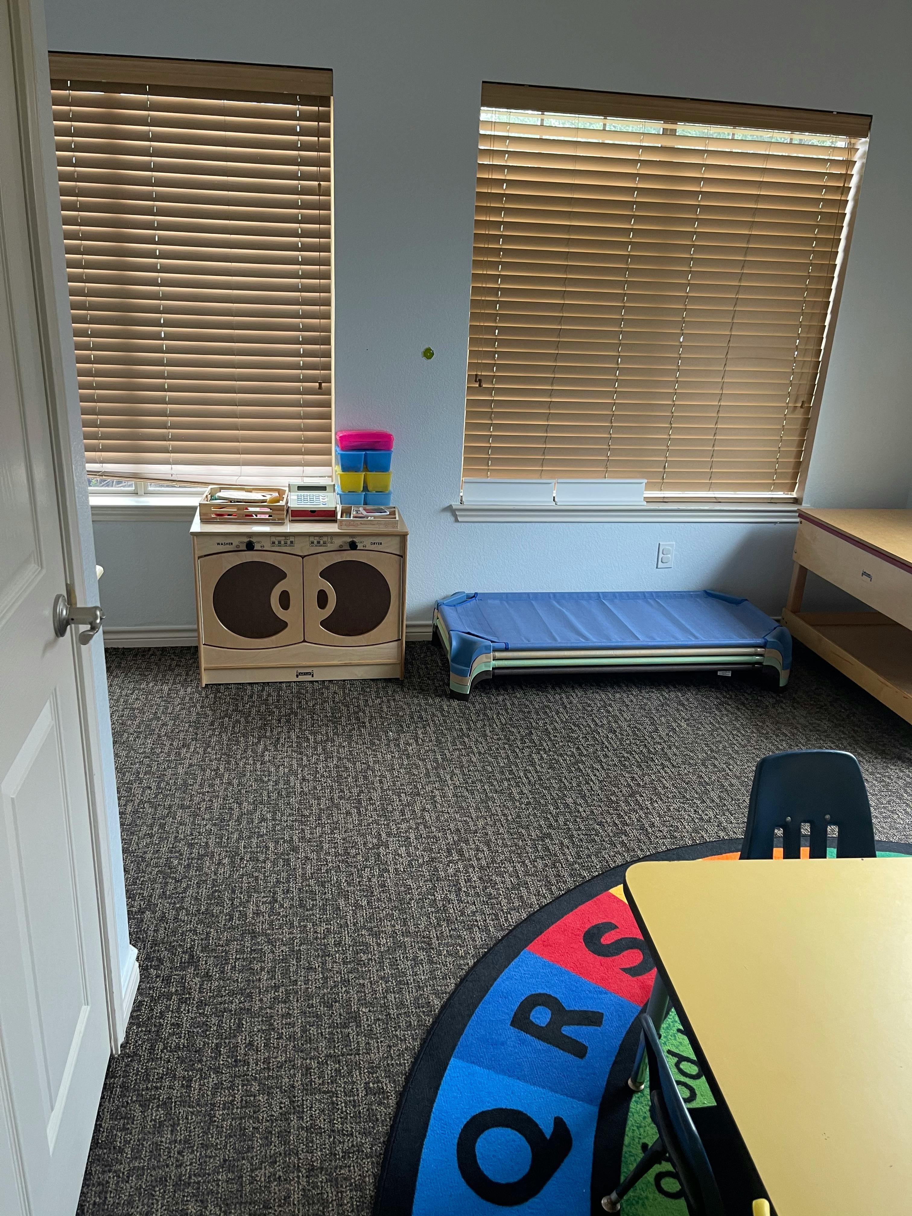 Classroom with windows, small bed, and alphabet rug