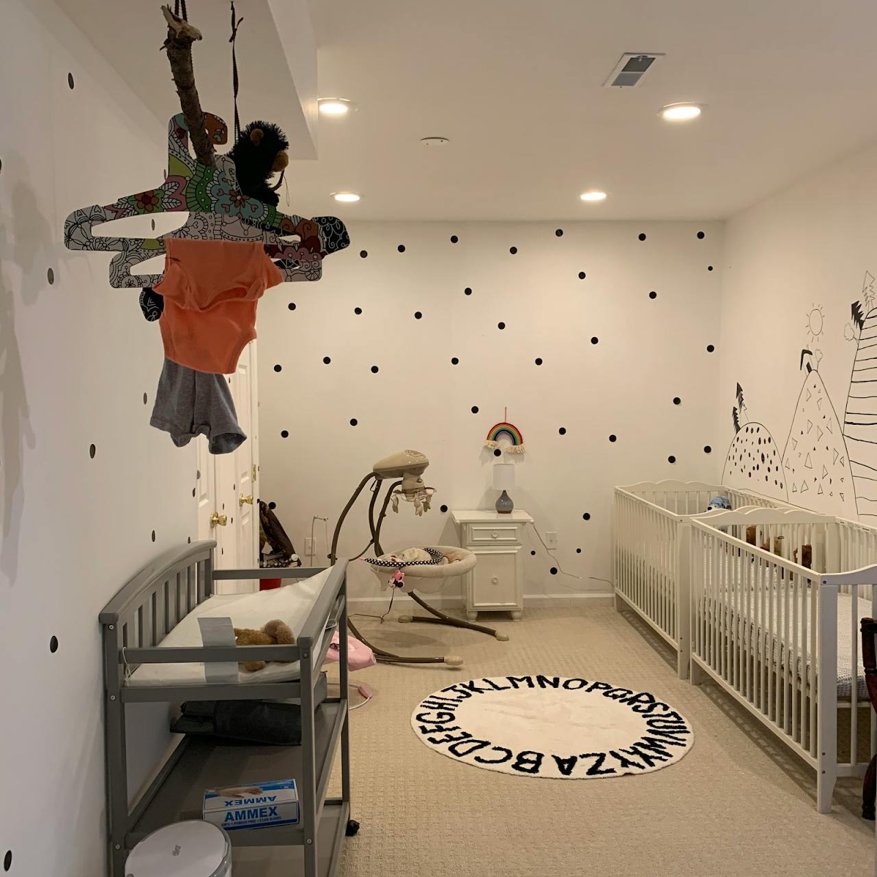Nursery room with two cribs, a changing table, and a baby swing