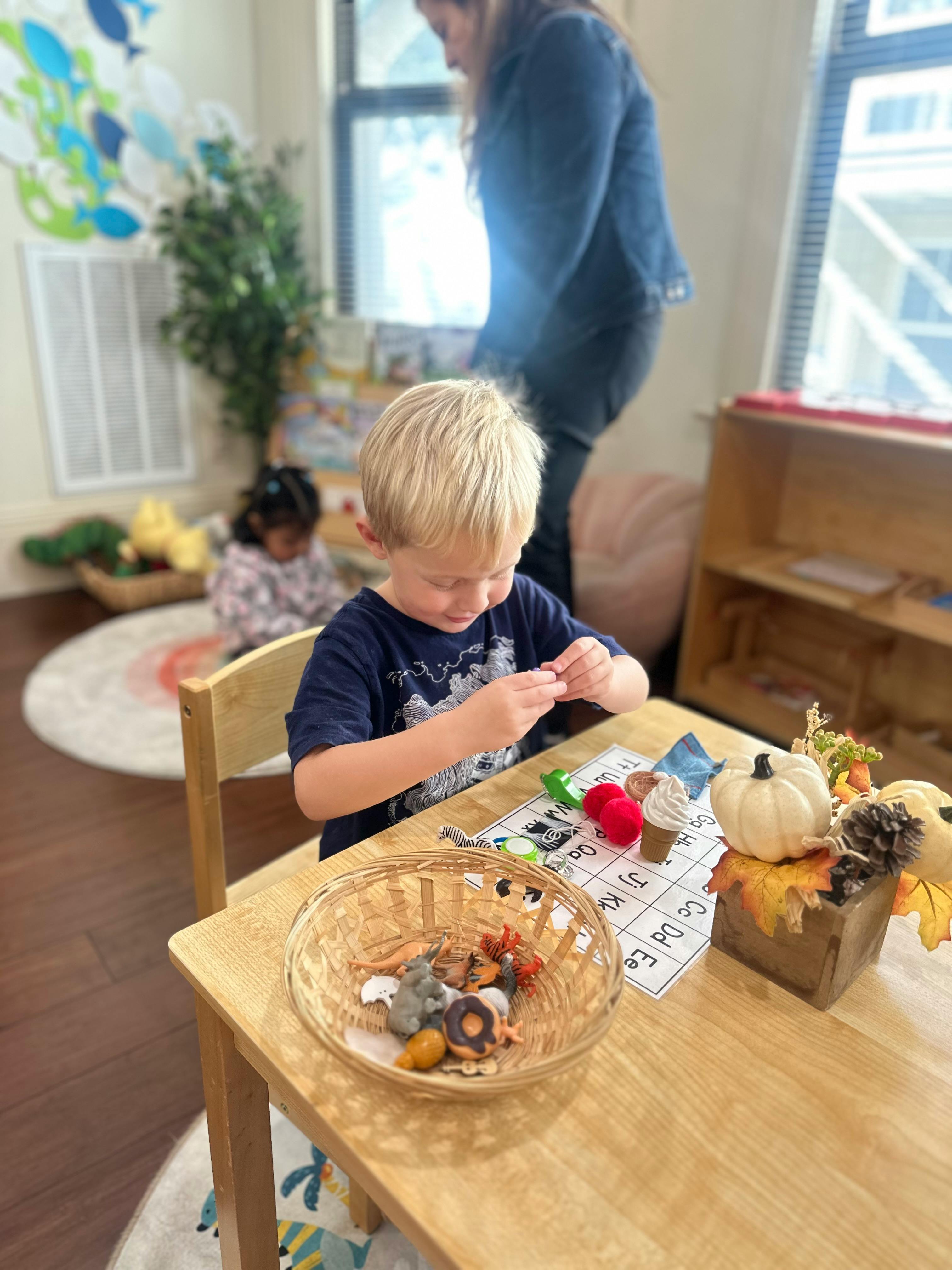 Child playing with small objects at a table in a classroom