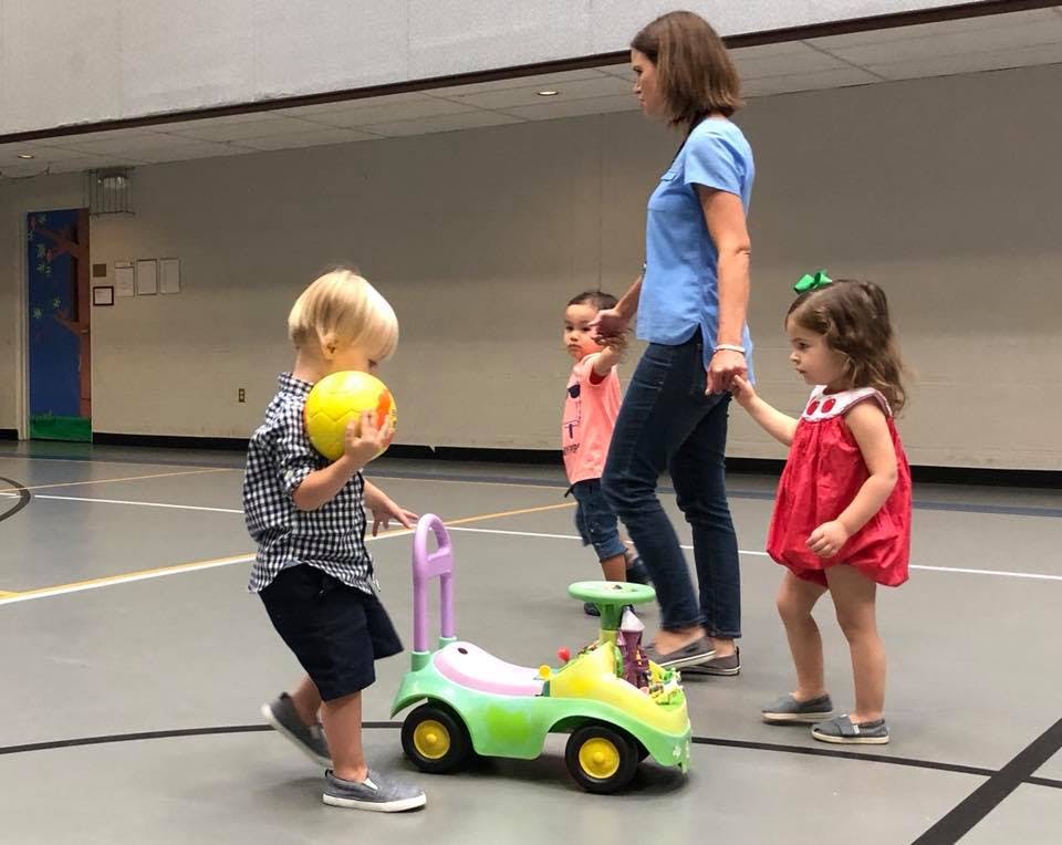 Person with three children in a gym, one child holding a ball