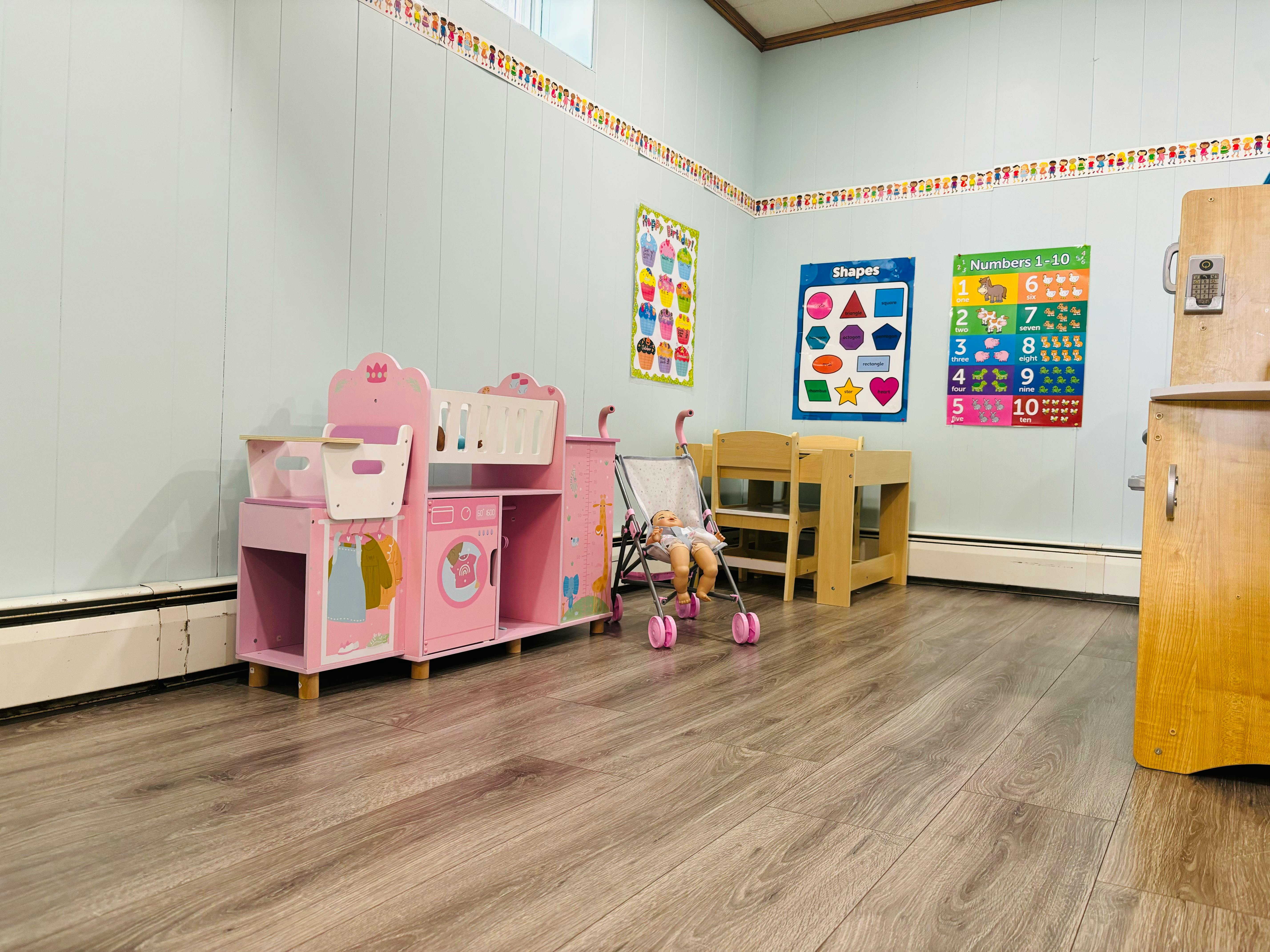 Playroom with pink toy kitchen, doll stroller, and wooden table and chairs