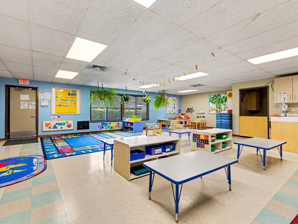 Empty classroom with small tables and a colorful alphabet rug