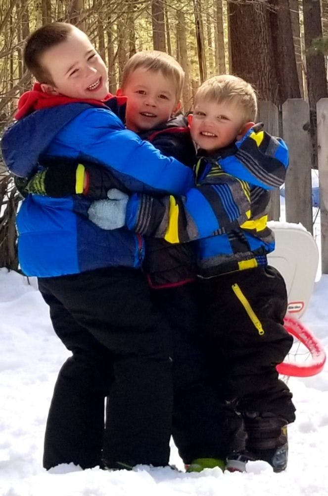 Three children in winter coats hugging in the snow