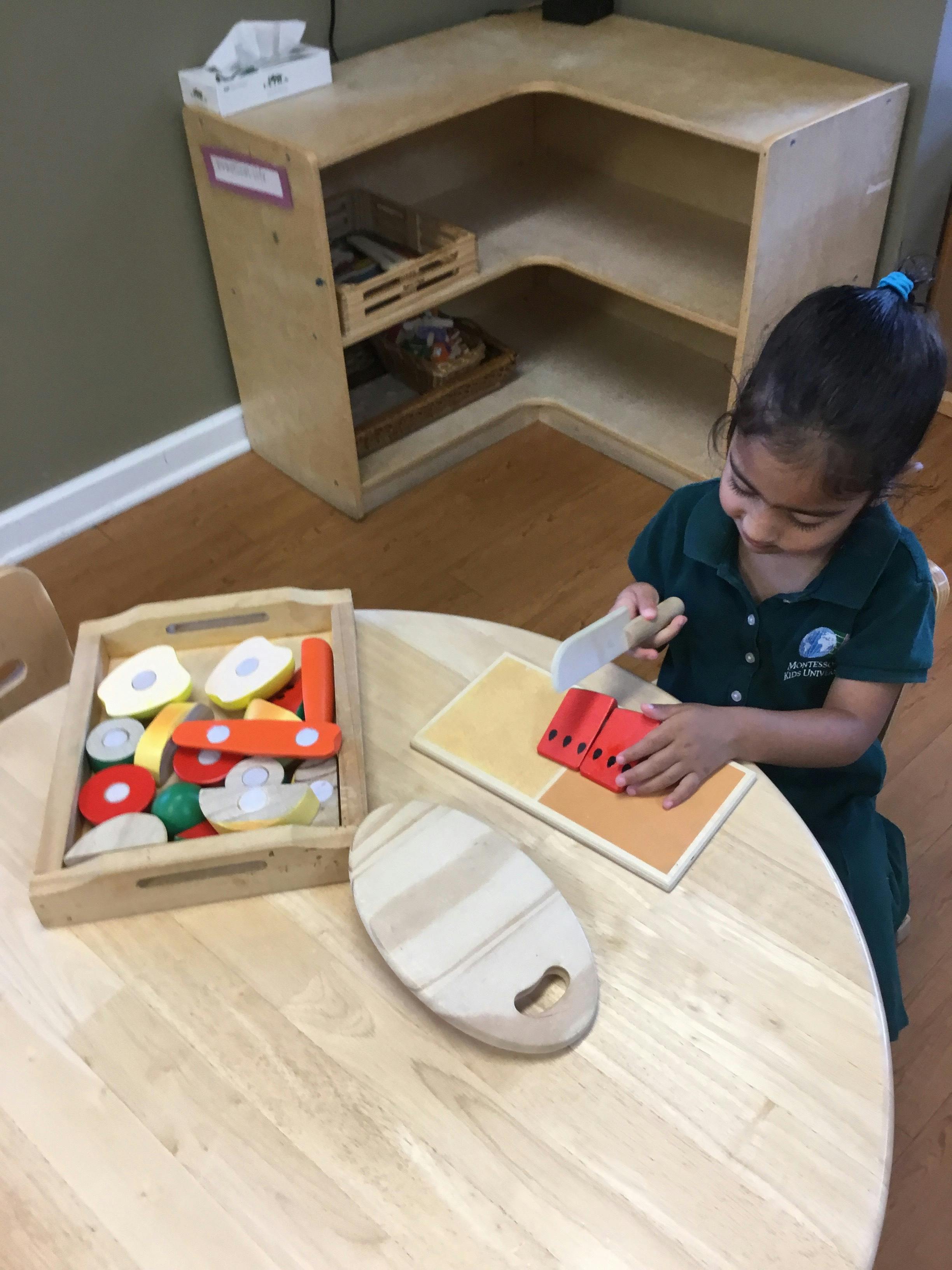 Child playing with toy food and cutting board at a table