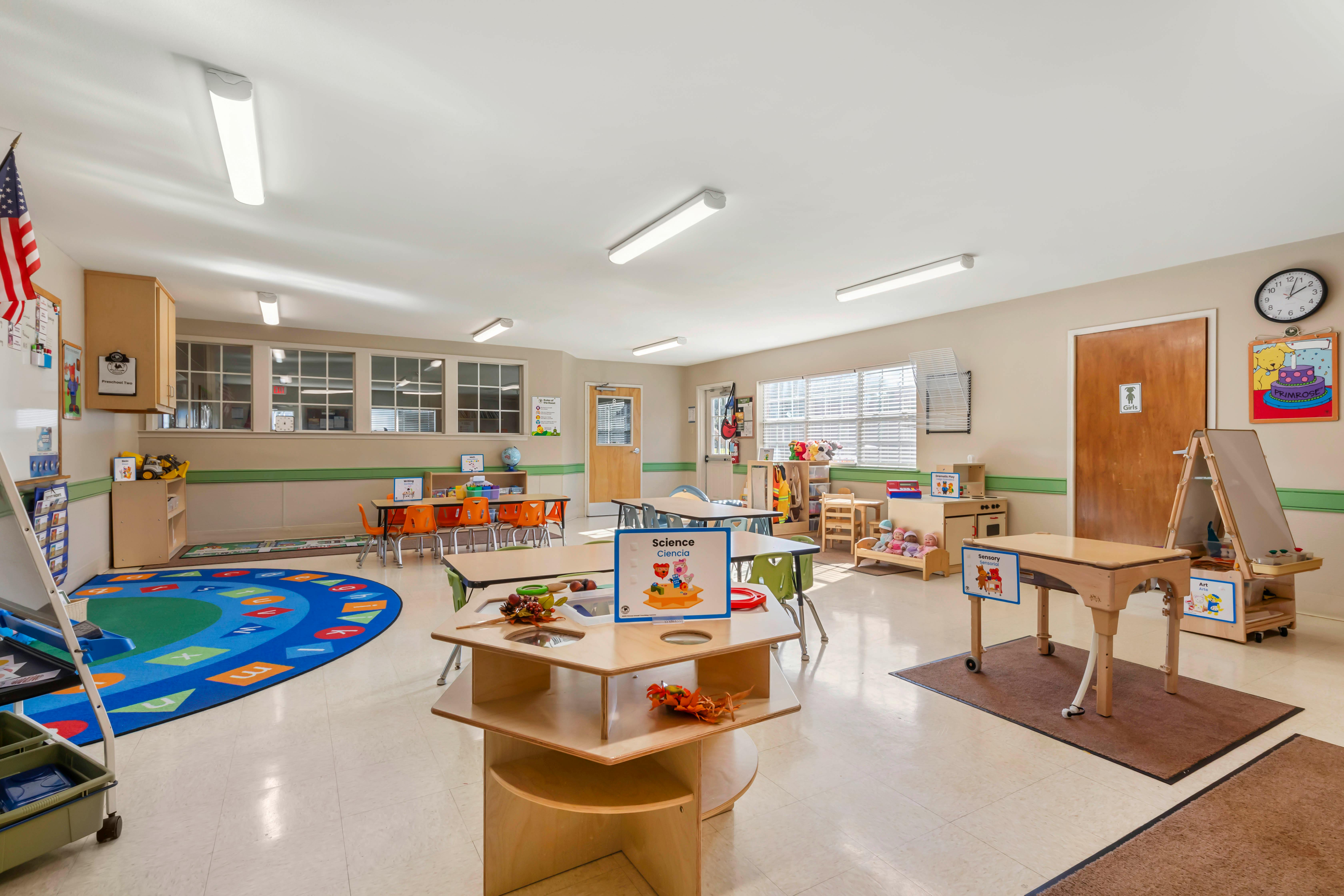 Empty preschool classroom with activity tables, chairs, and rugs