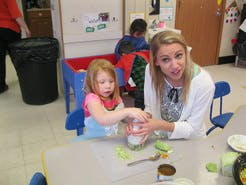 Adult and child at a table, child holding a jar