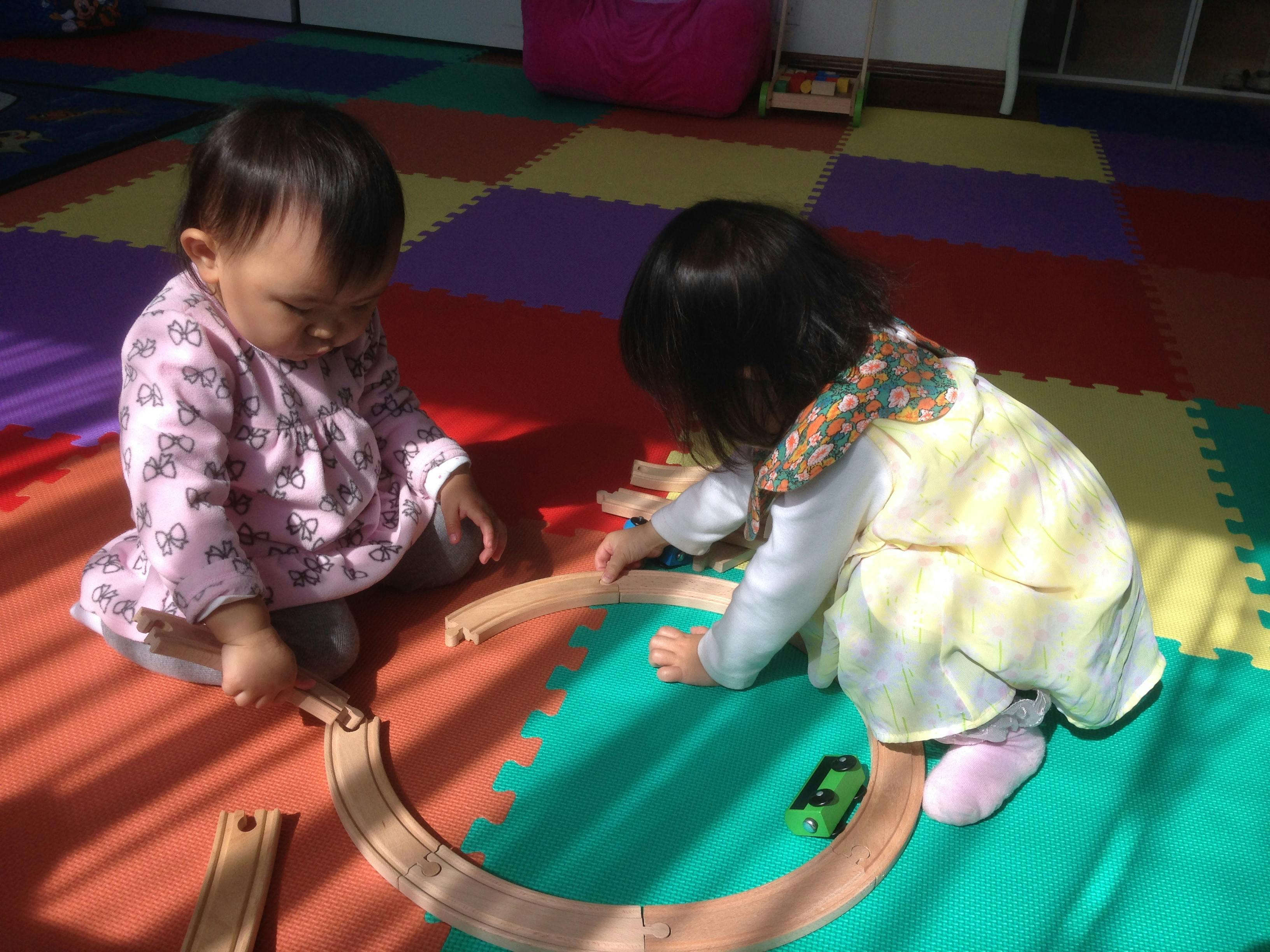 Two children playing with a wooden train set on a colorful mat