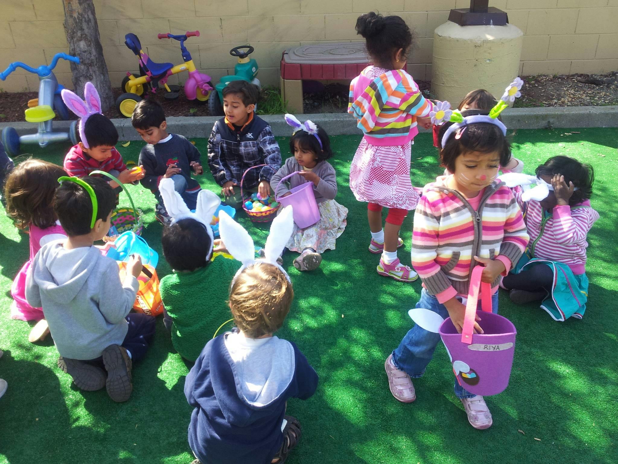 Children wearing bunny ears and holding baskets on a green surface