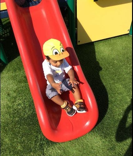 Child in a yellow hat sitting on a red slide