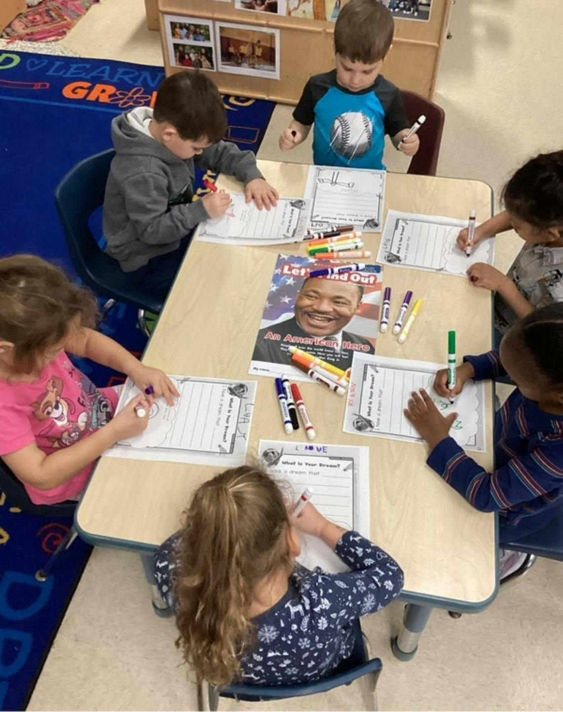 Children writing at a table with markers and a magazine about Martin Luther King Jr