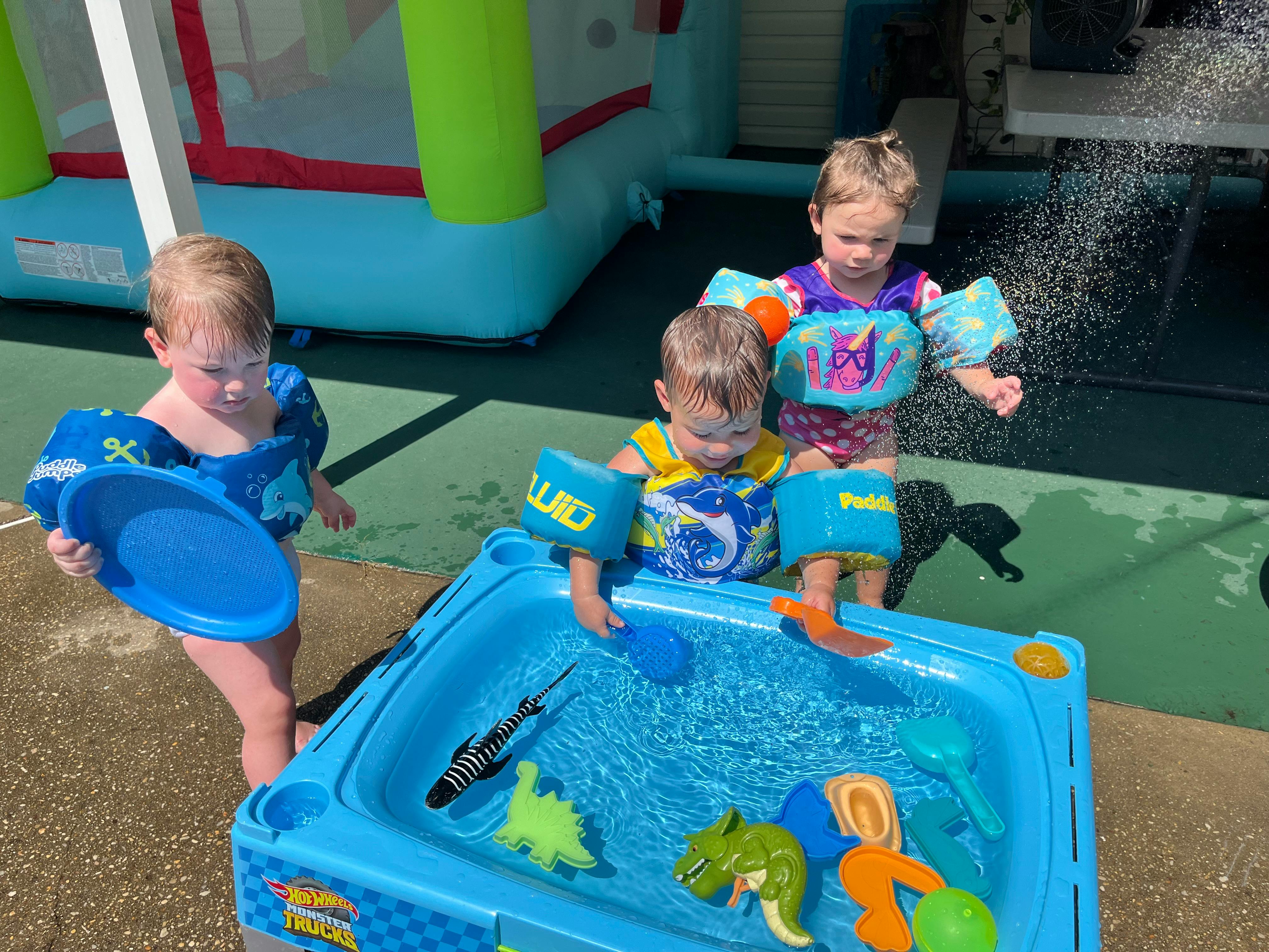 Three children playing with water in a blue water table