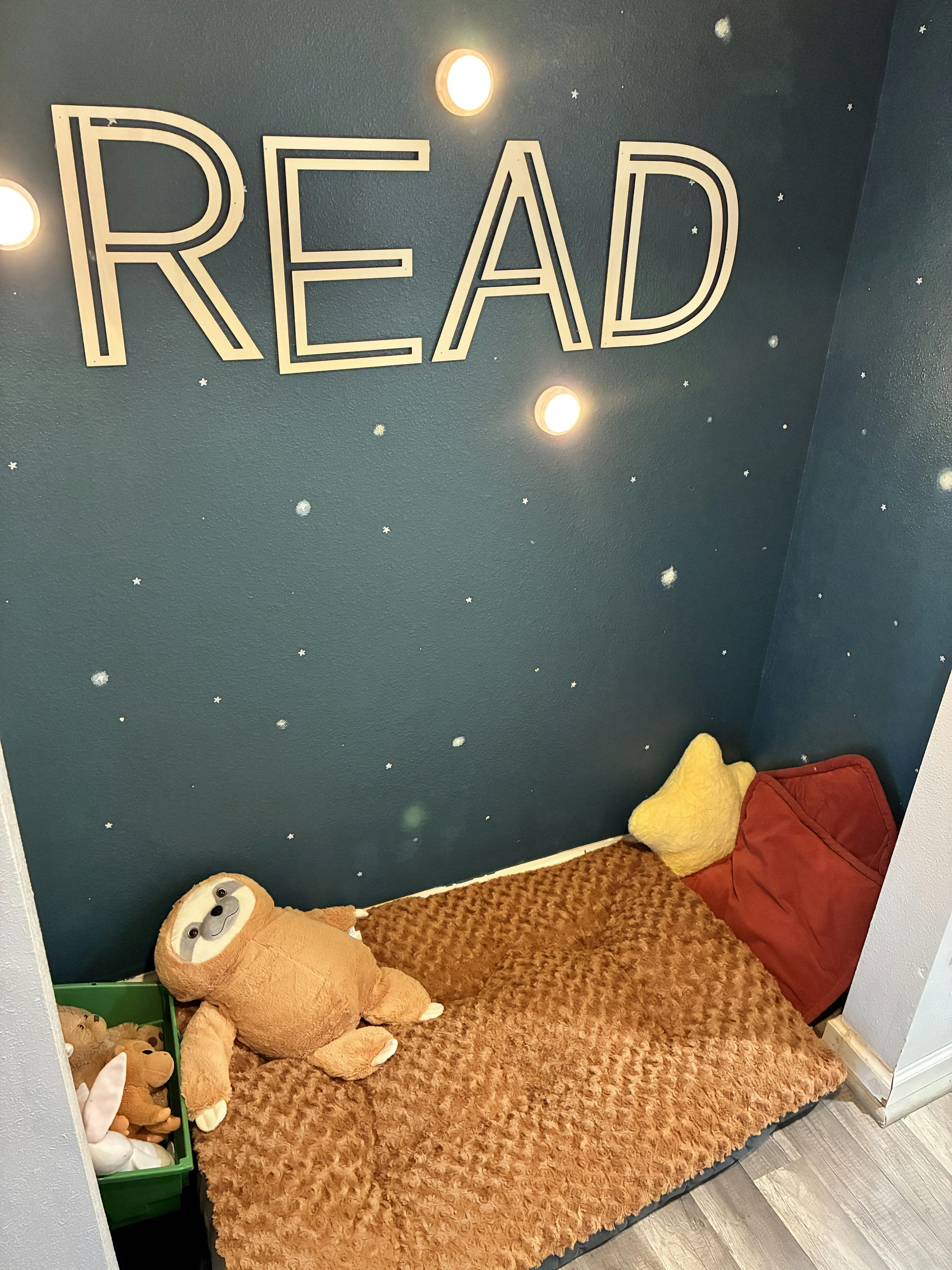 Reading nook with a brown sloth plush toy, red and yellow cushions, and the word "READ"