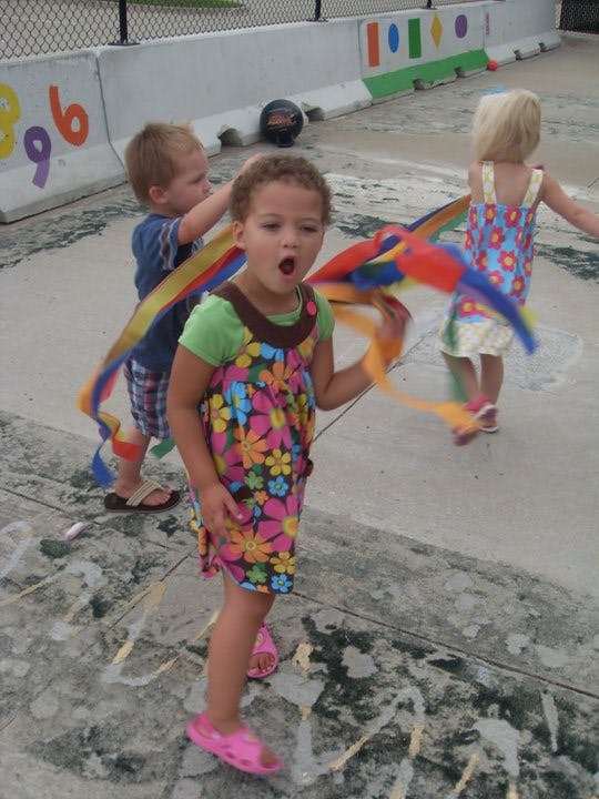 Child holding a colorful ribbon wand with two other children nearby