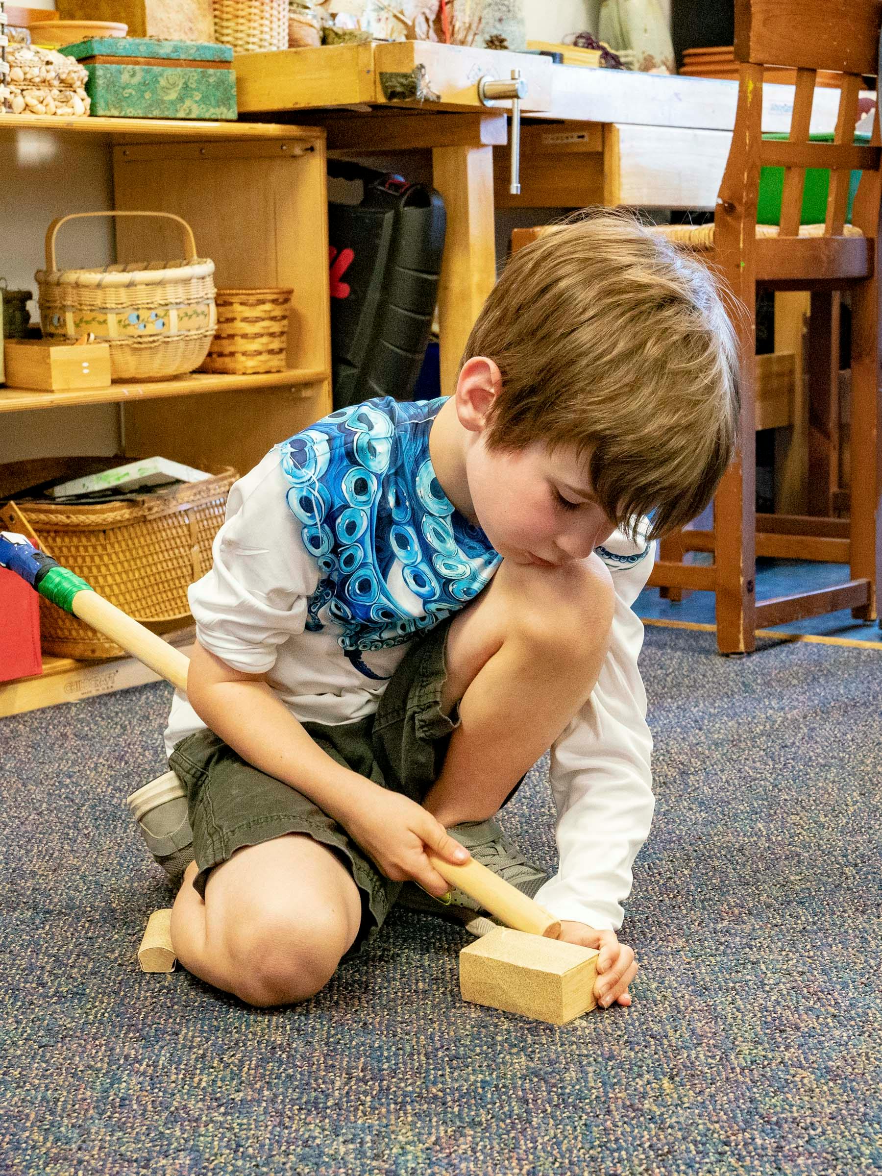 Child kneeling on floor, holding a wooden stick to a wooden block