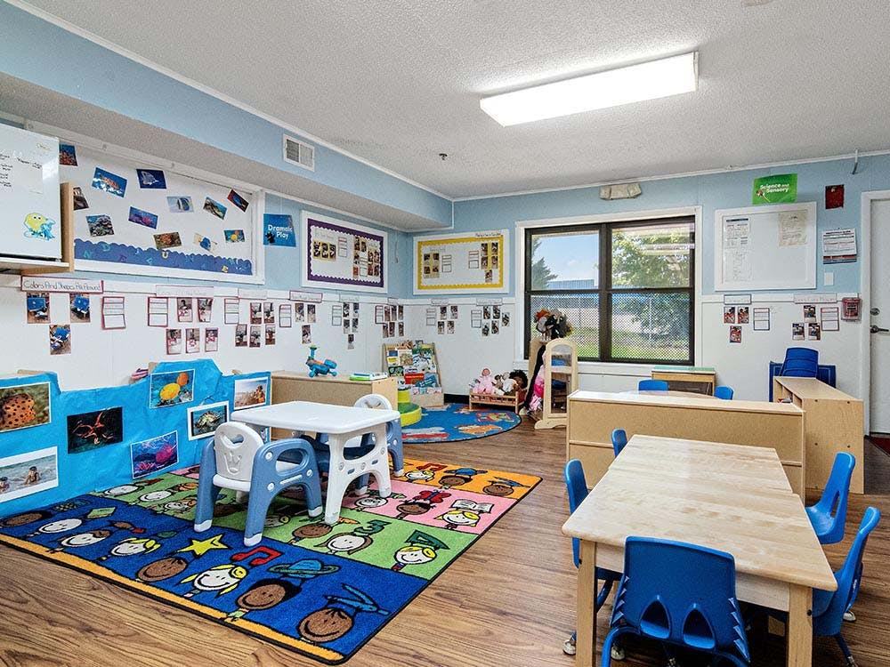 Classroom with child-sized tables and chairs, colorful rugs, and wall decorations