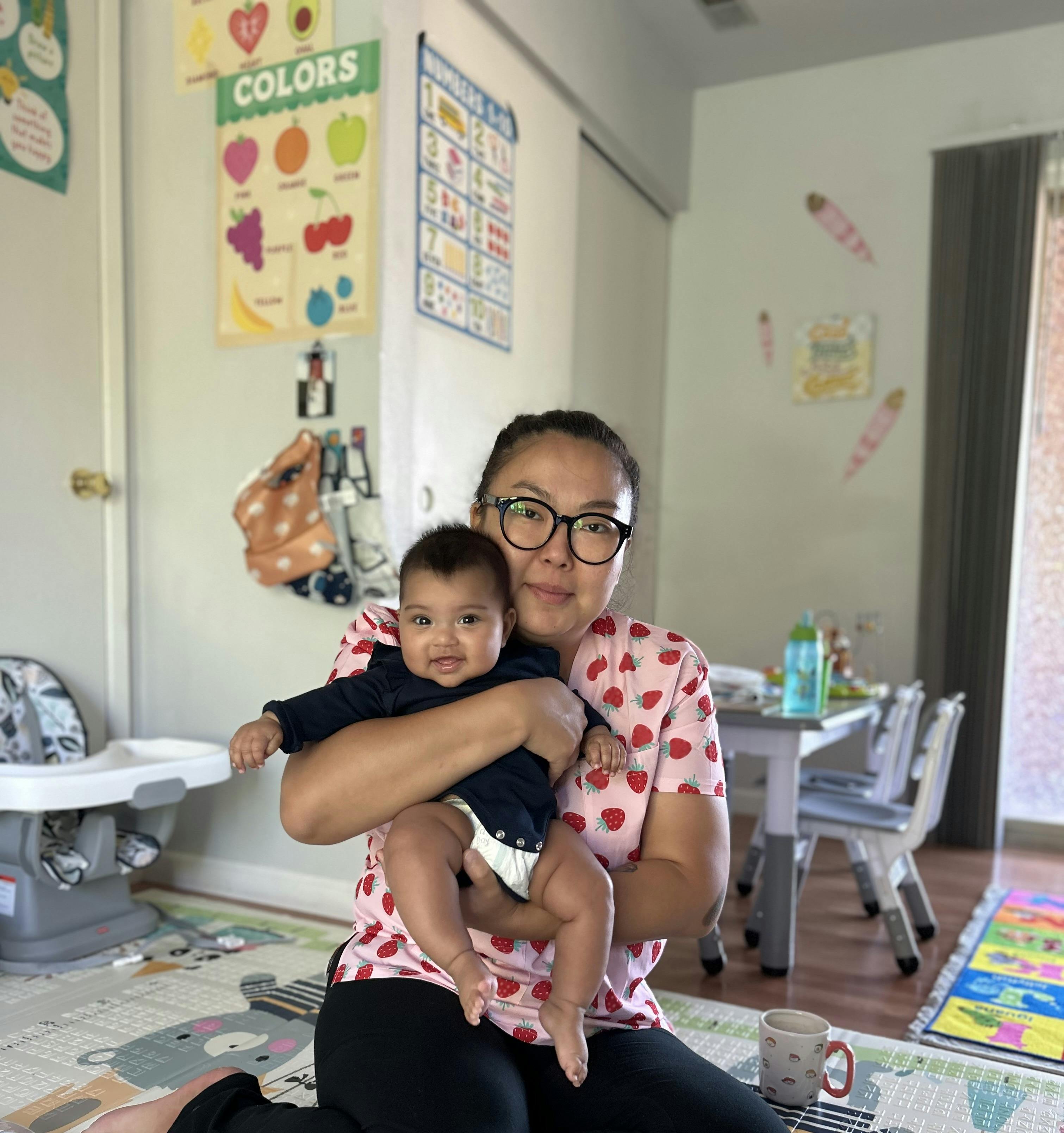 Person holding a child in a room with a "COLORS" poster