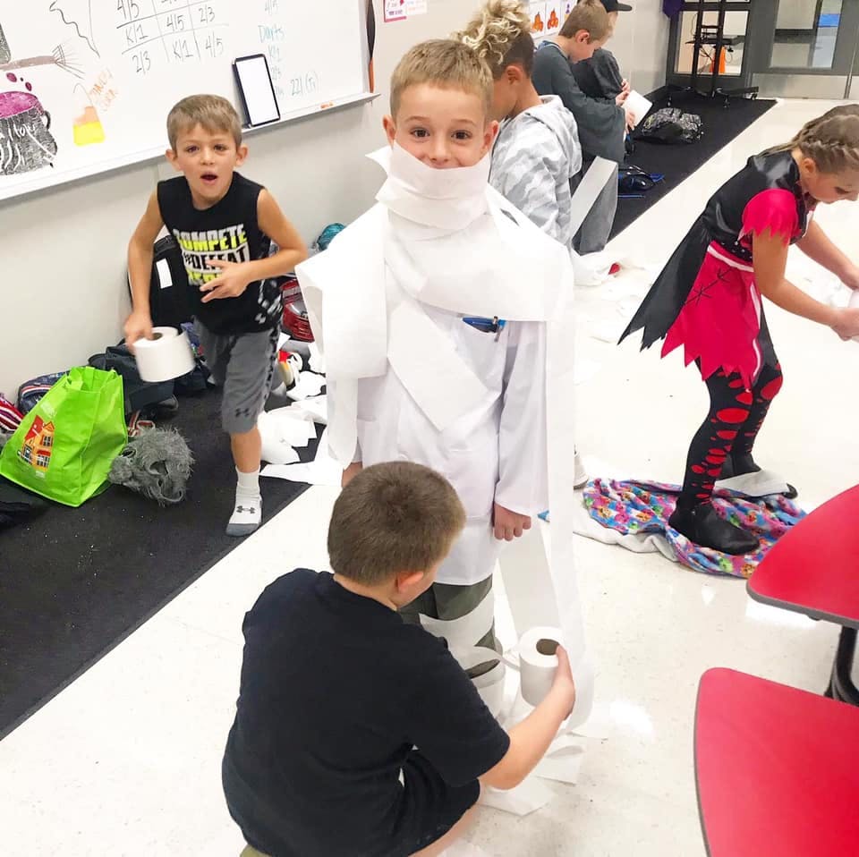 Children wrapping a child in toilet paper in a classroom