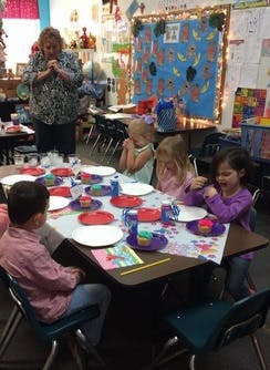 Adult and children at a table with plates and cupcakes in a classroom