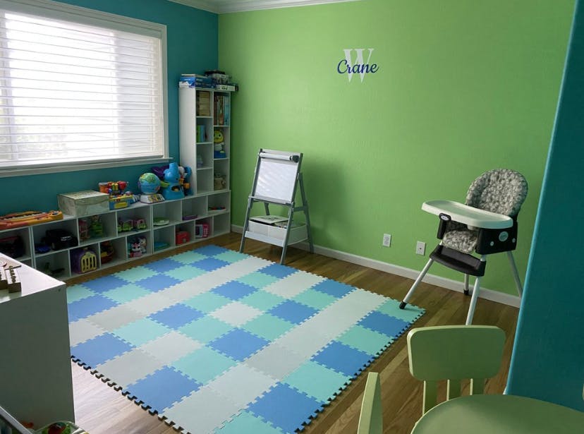 Playroom with a checkered mat, shelves, easel, and high chair