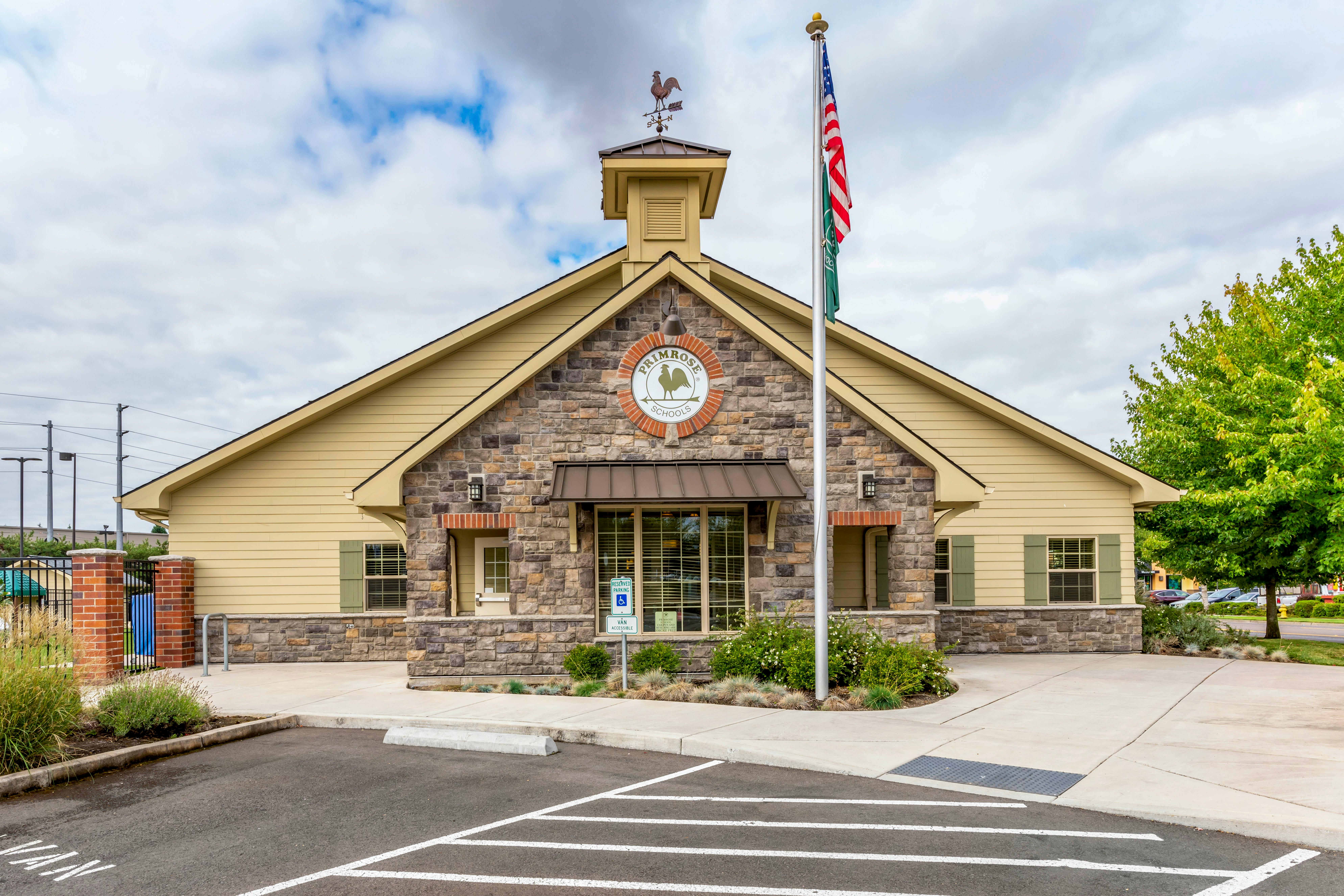 A beige building with stone facade, a cupola, an American flag, and a sign that says Primrose Schools