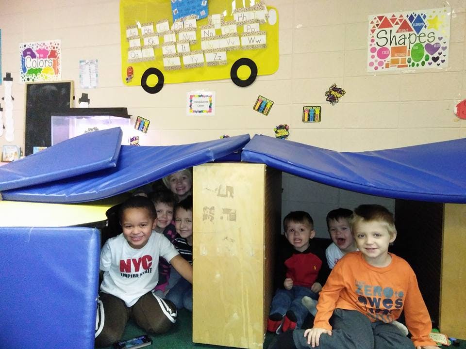 Children playing in a fort made of blue mats and cardboard boxes