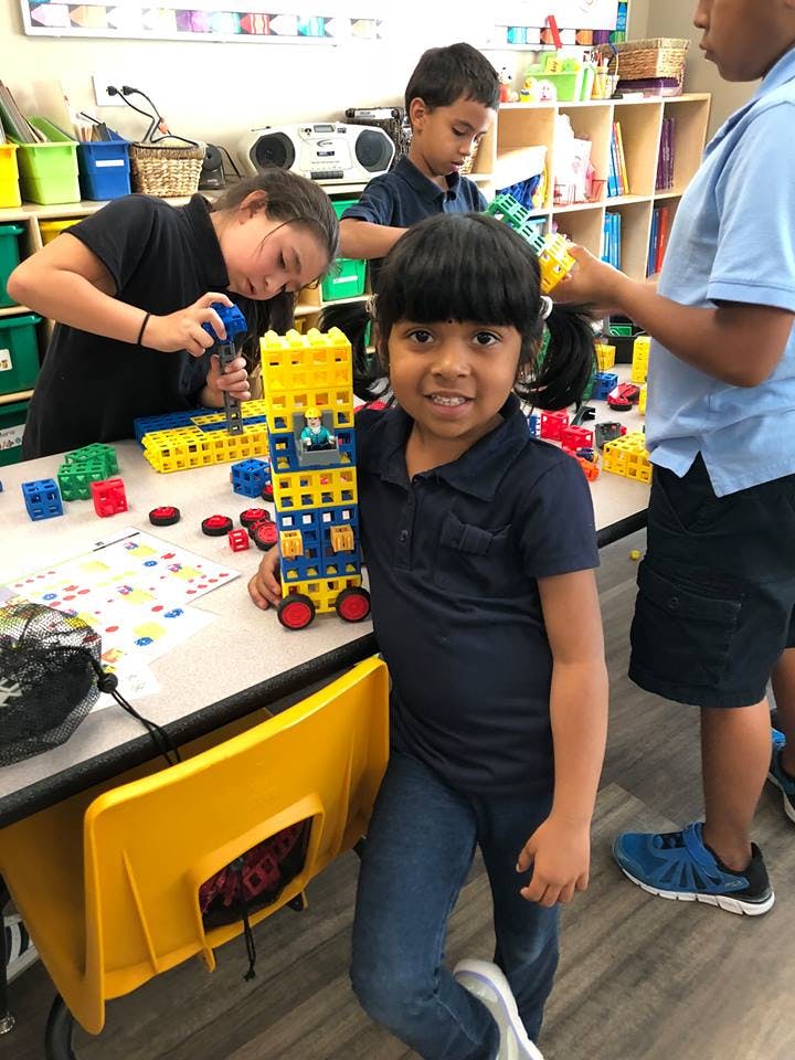 Child holding a toy made of building blocks, other children playing in background