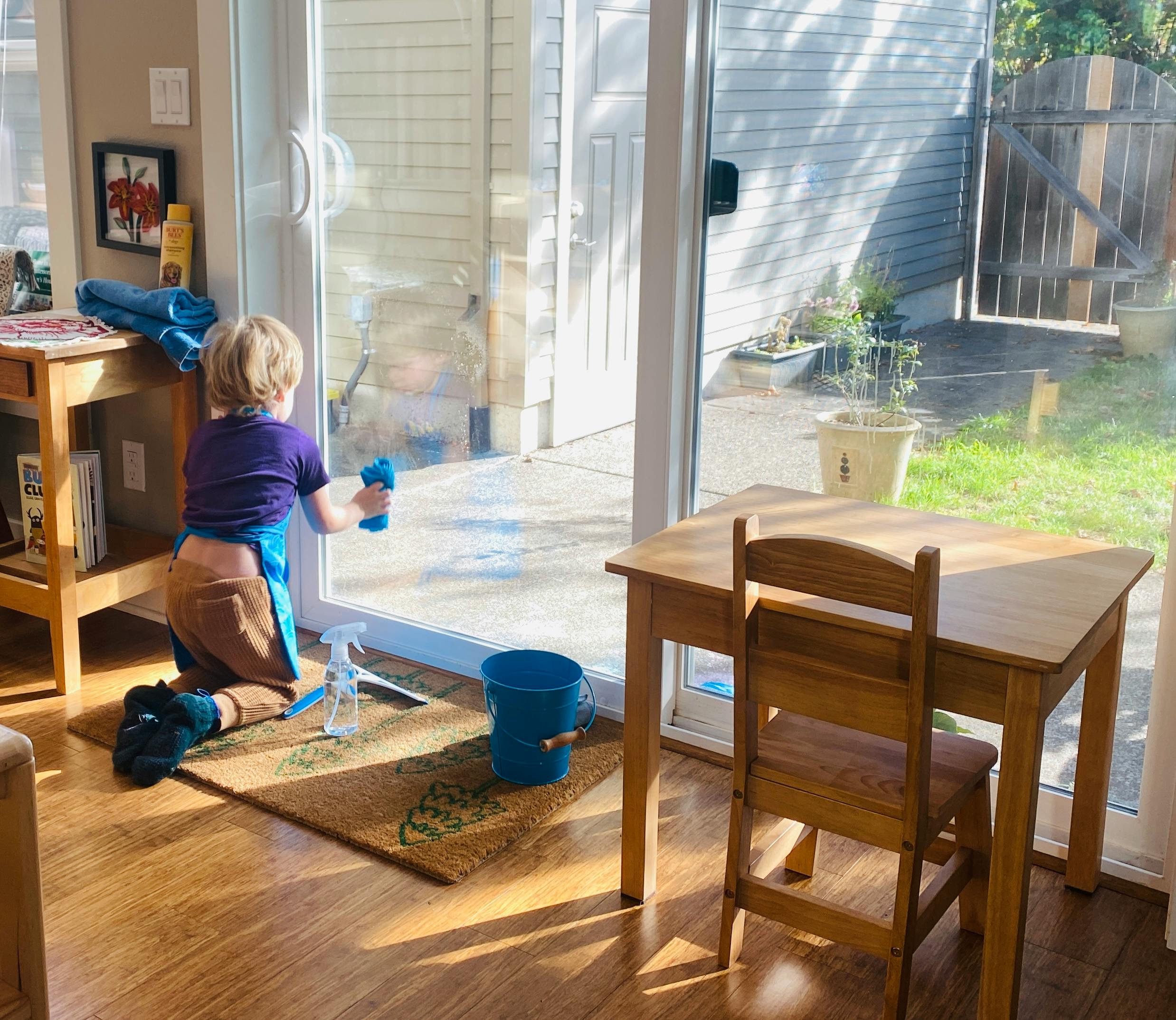 Child kneeling and cleaning a glass door