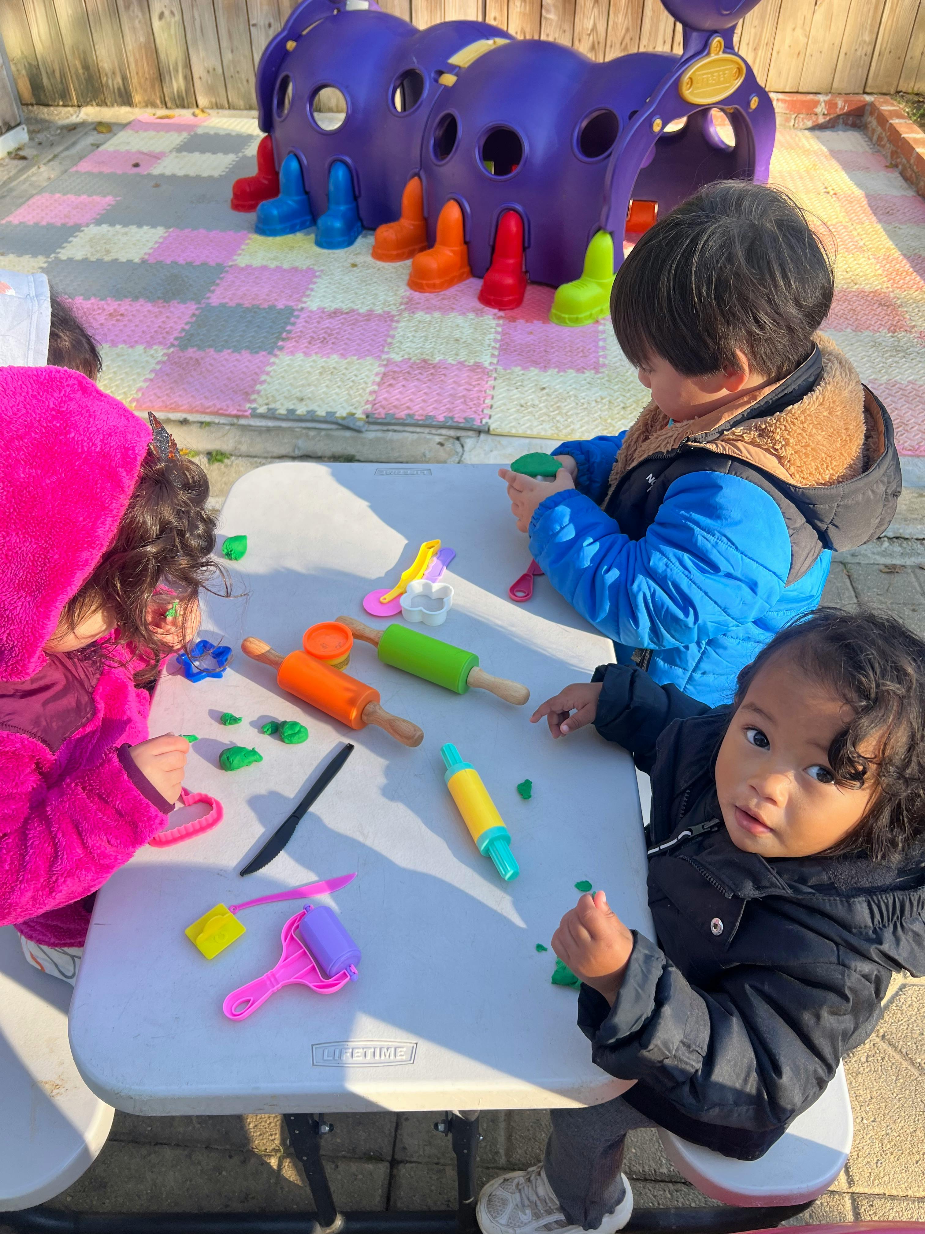 Children playing with modeling clay and tools at a table outdoors