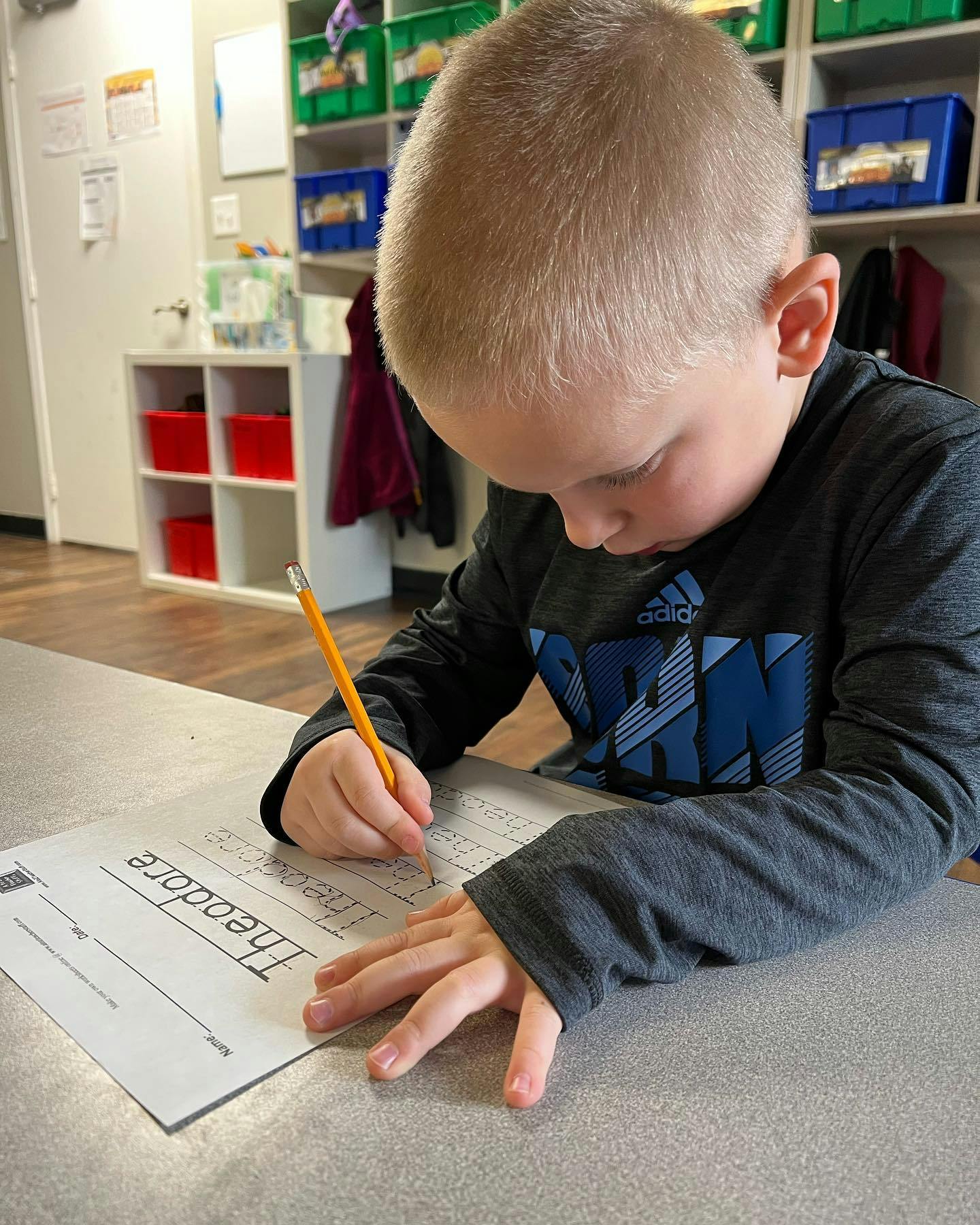 Child writing "Theodore" on a paper with a pencil
