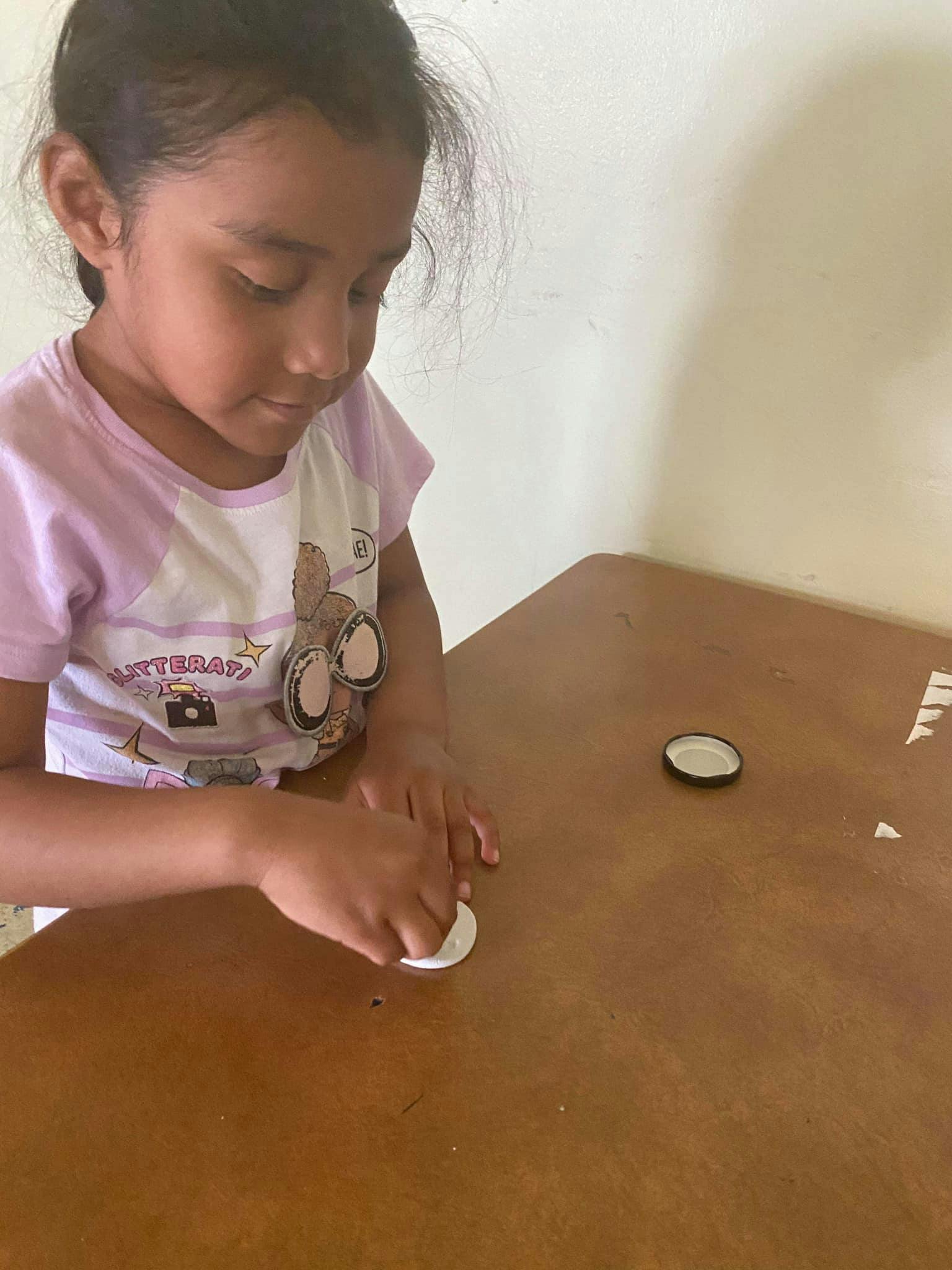 Child pressing a white bottle cap onto a surface