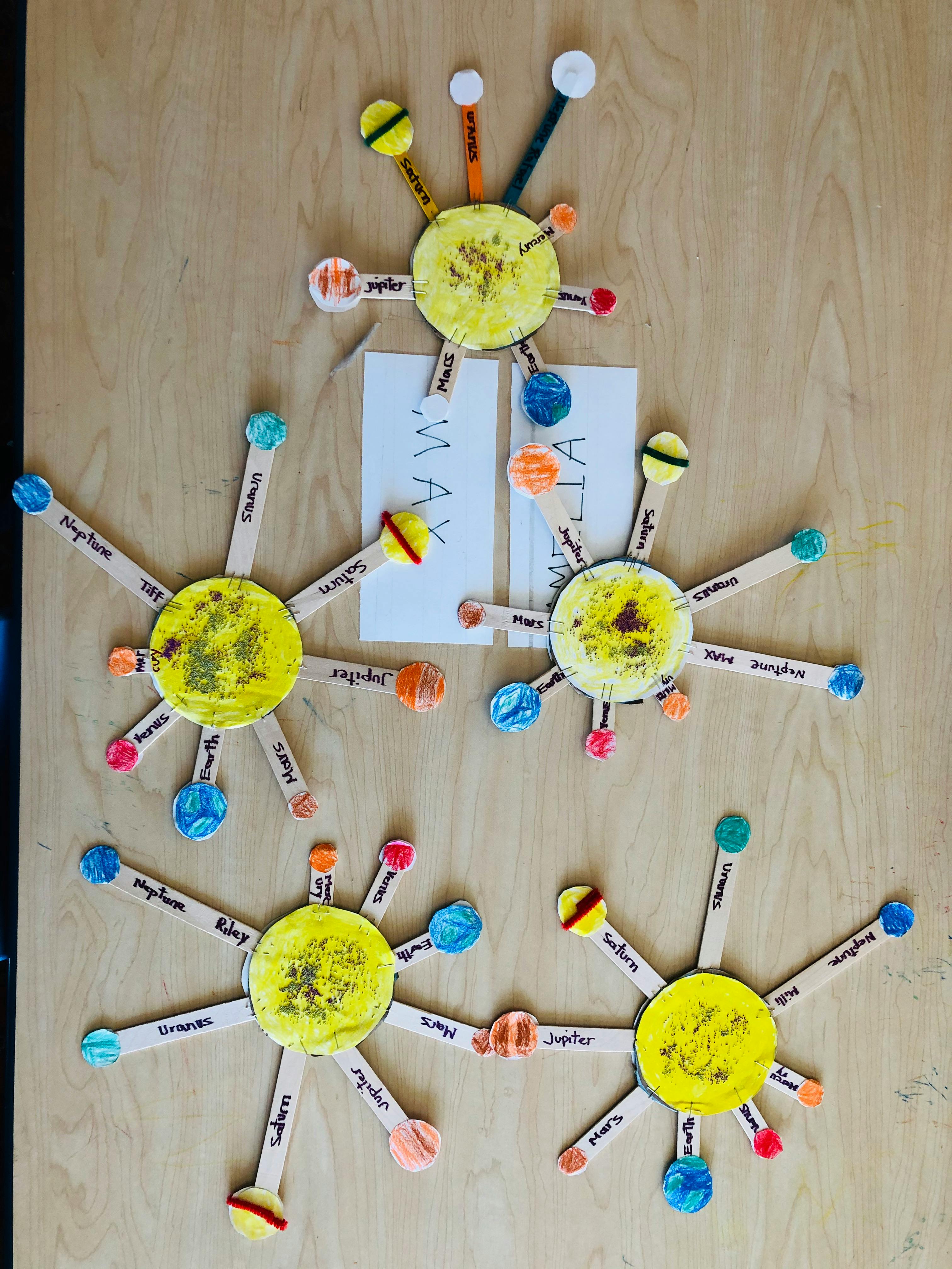 Multiple solar system crafts made from yellow circles and craft sticks with painted planets