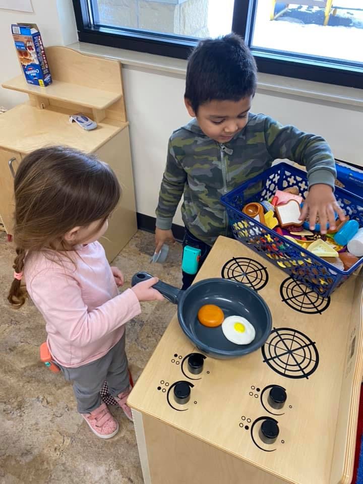 Two children playing with a toy kitchen and food